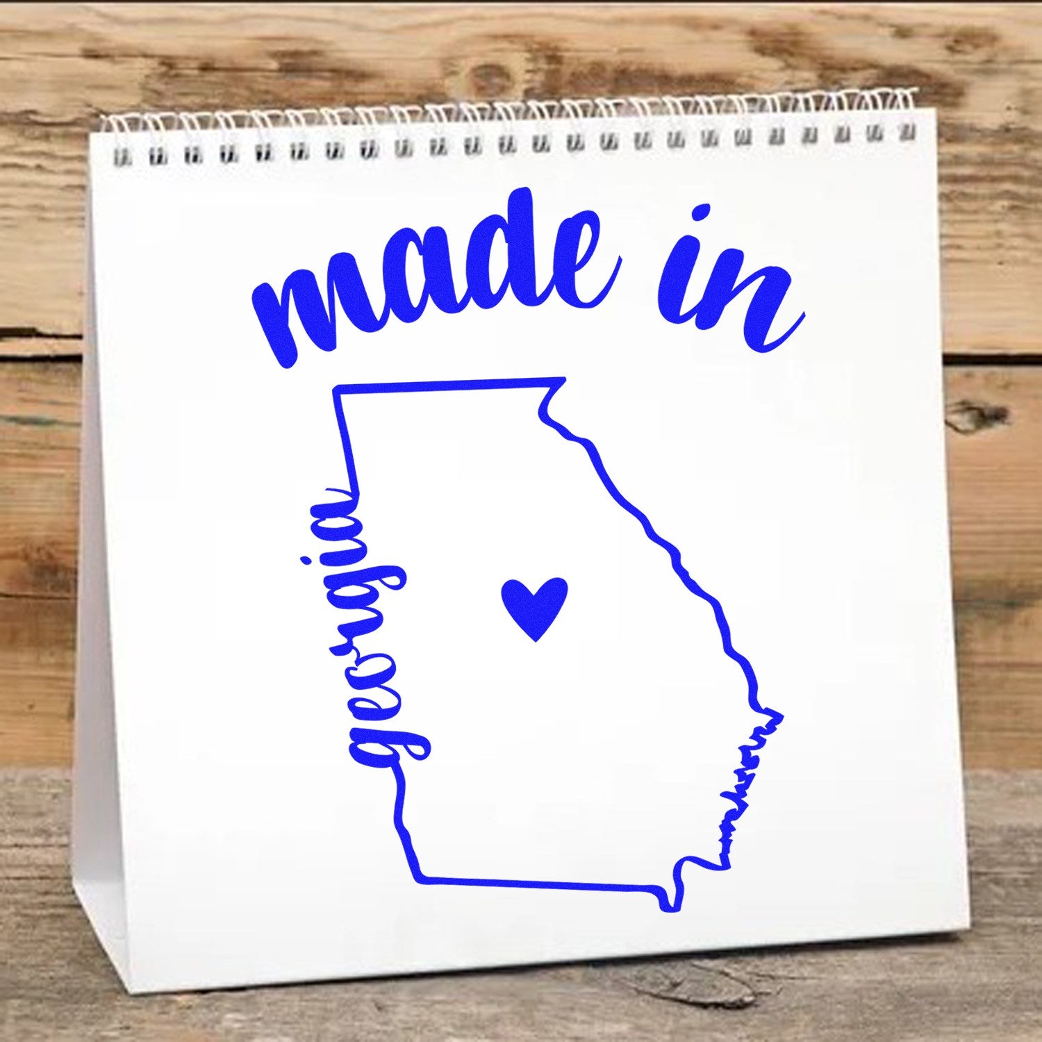 Made with Love in Georgia Rubber Stamp featuring a blue outline of Georgia with a heart, and 'made in' text on a spiral-bound notepad background.