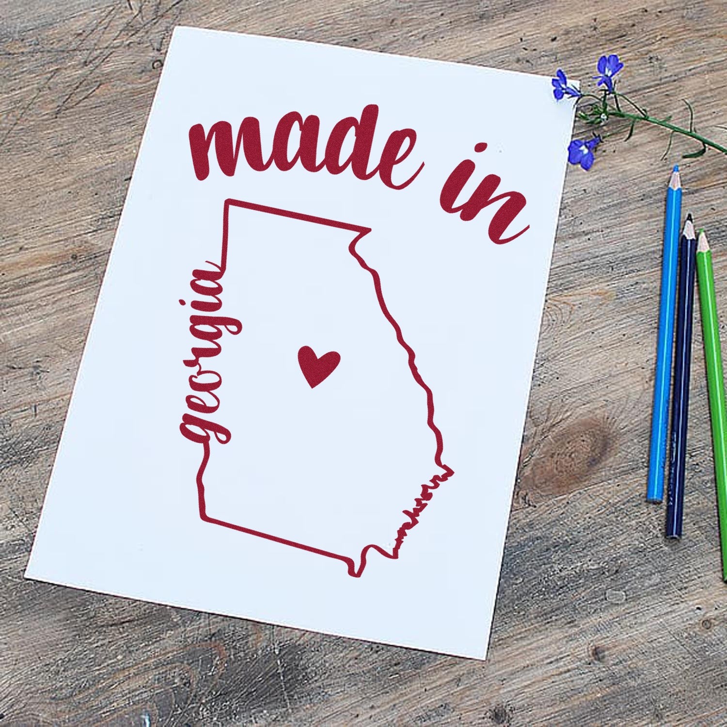 Made with Love in Georgia Rubber Stamp featuring a red outline of Georgia with a heart, 'made in' text, and colored pencils on a wooden surface.