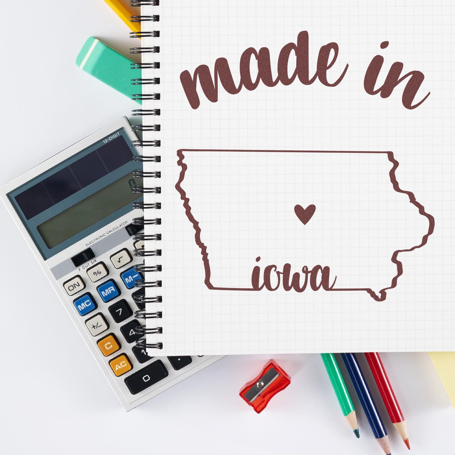 Made with Love in Iowa Rubber Stamp on notebook with Iowa map and heart design, surrounded by colorful stationery including a calculator, pencils, and eraser.