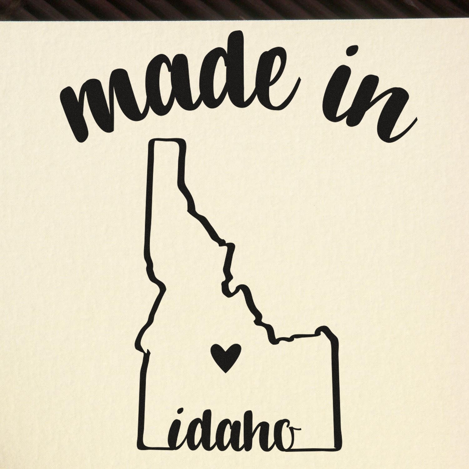 Made in Idaho Stamp Pre-Inked featuring a black outline of Idaho with a heart, and 'made in Idaho' text above and below, on a beige background.