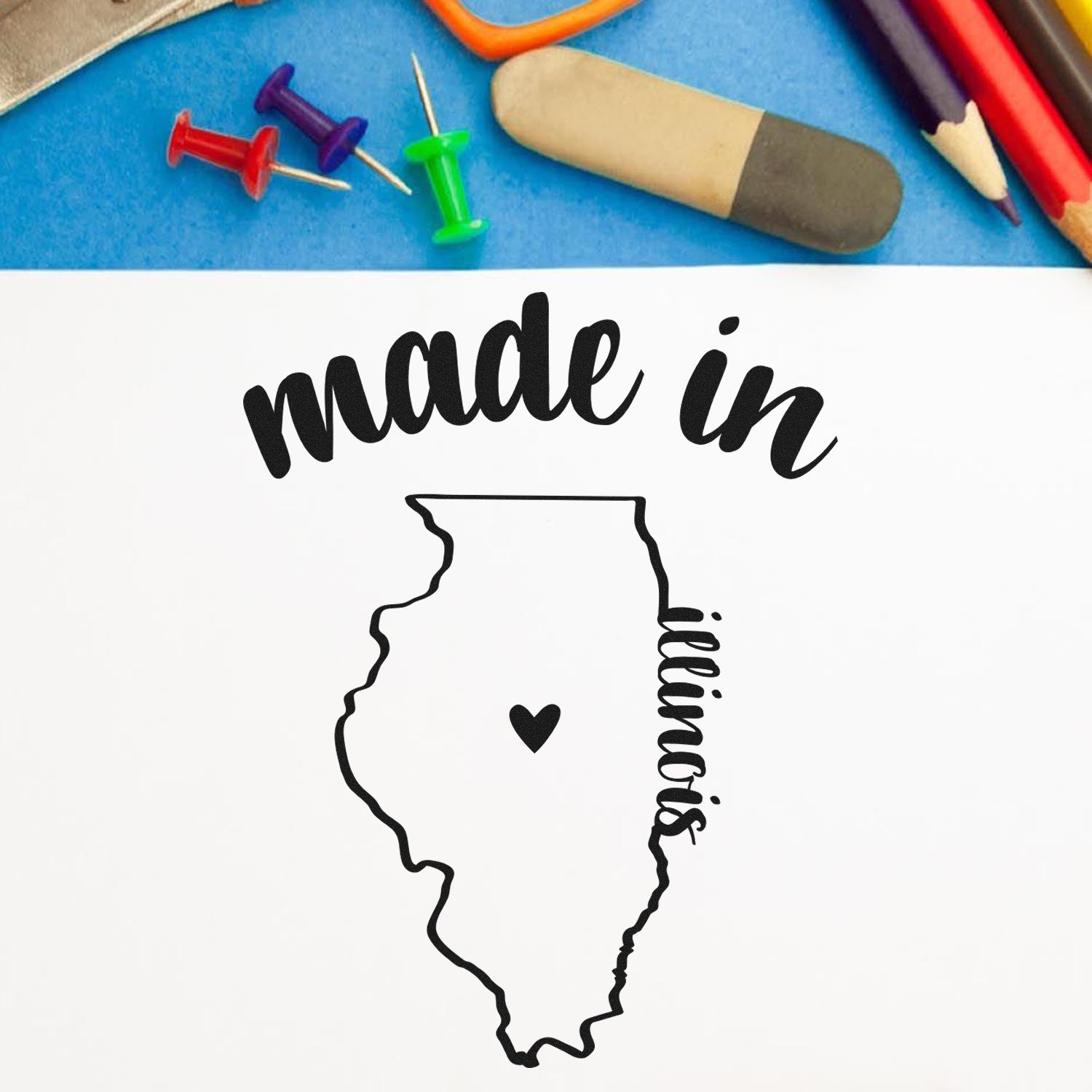 Self-Inking Handmade with Love in Illinois Stamp featuring a heart within the state outline, surrounded by colorful office supplies on a blue background. Perfect for crafts and gifts.