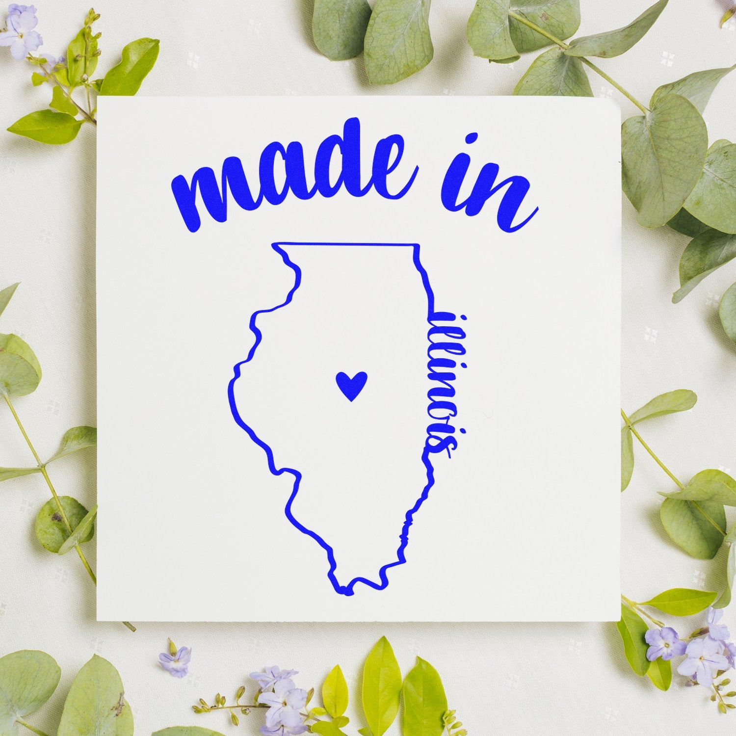 Made with Love in Illinois Rubber Stamp featuring a blue outline of Illinois with a heart, surrounded by green leaves and purple flowers on a white background.