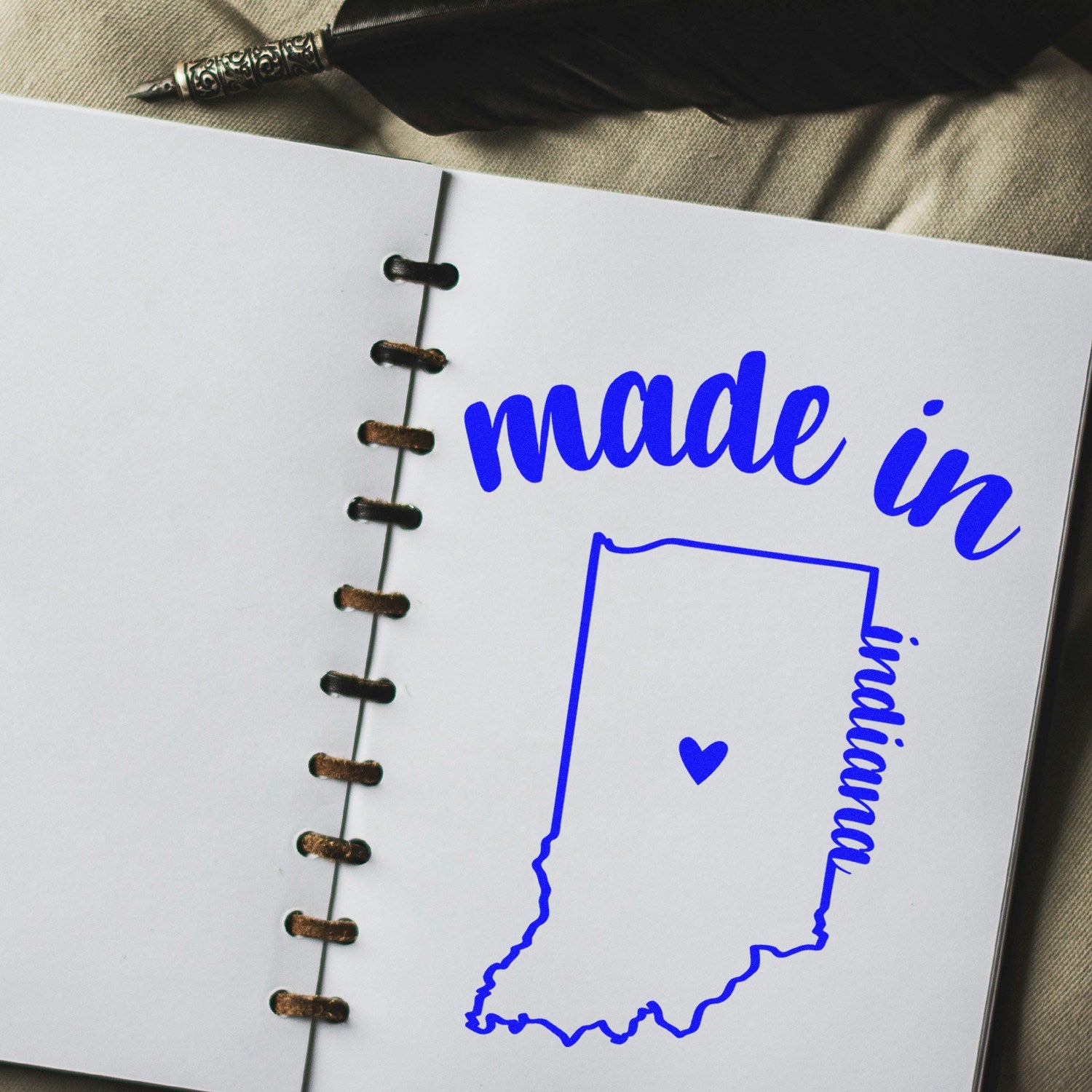 Made with Love in Indiana Rubber Stamp featuring a blue outline of Indiana with a heart, displayed on an open notebook with a pen nearby.