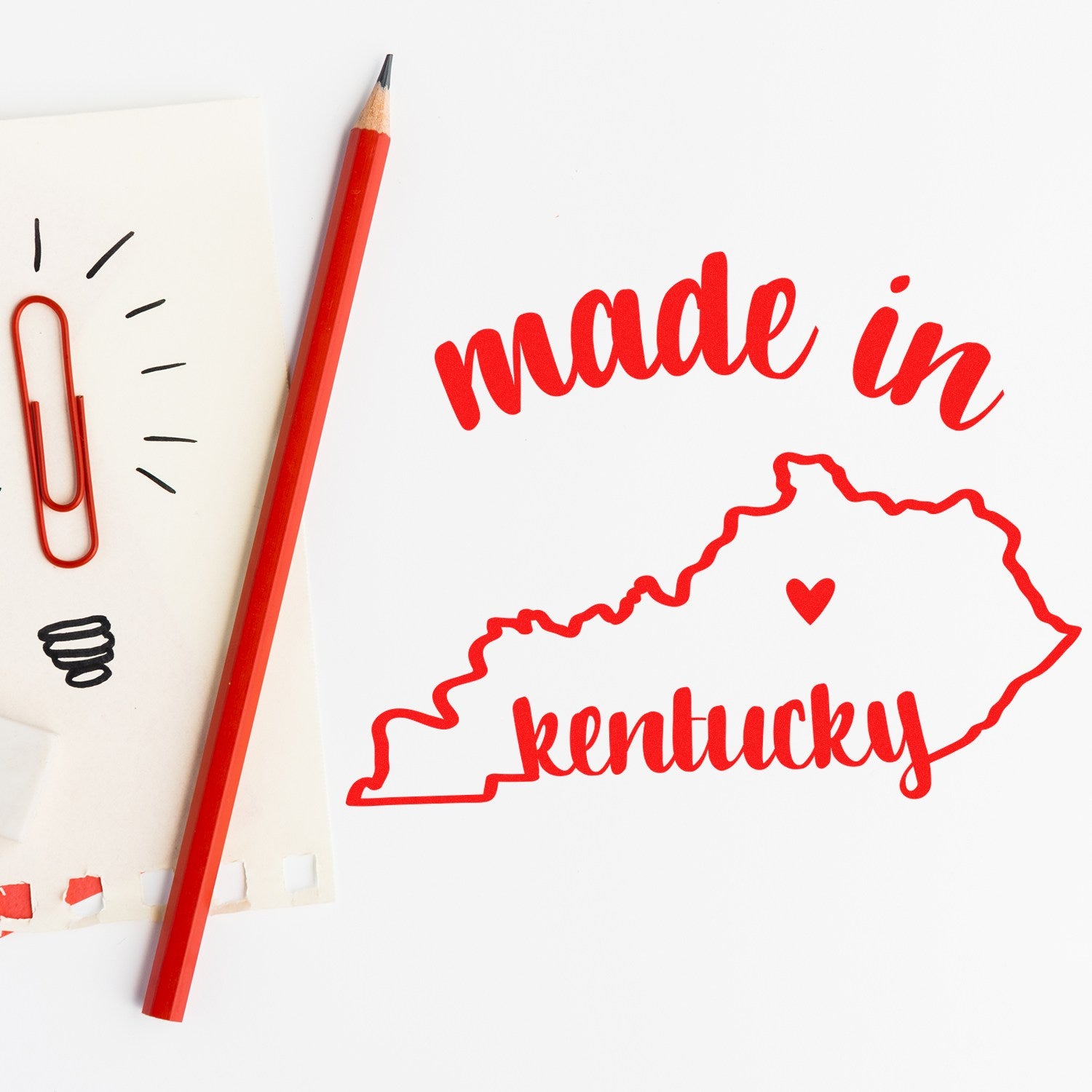 Self-Inking Handmade with Love in Kentucky Stamp featuring a red outline of Kentucky with 'made in' text, next to a red pencil and paper with a lightbulb sketch.