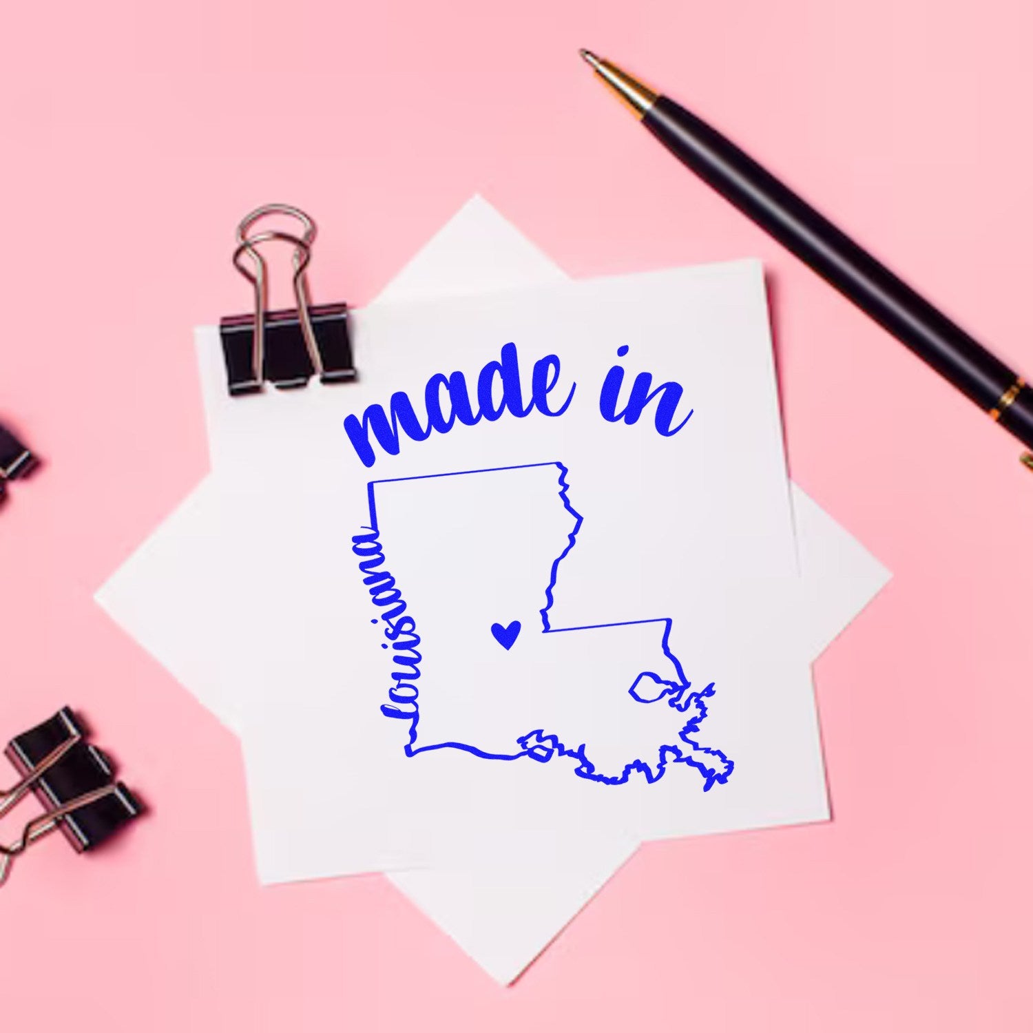 Made with Love in Louisiana Rubber Stamp featuring a blue outline of Louisiana with 'made in' text, displayed on a pink background with a pen and clips.