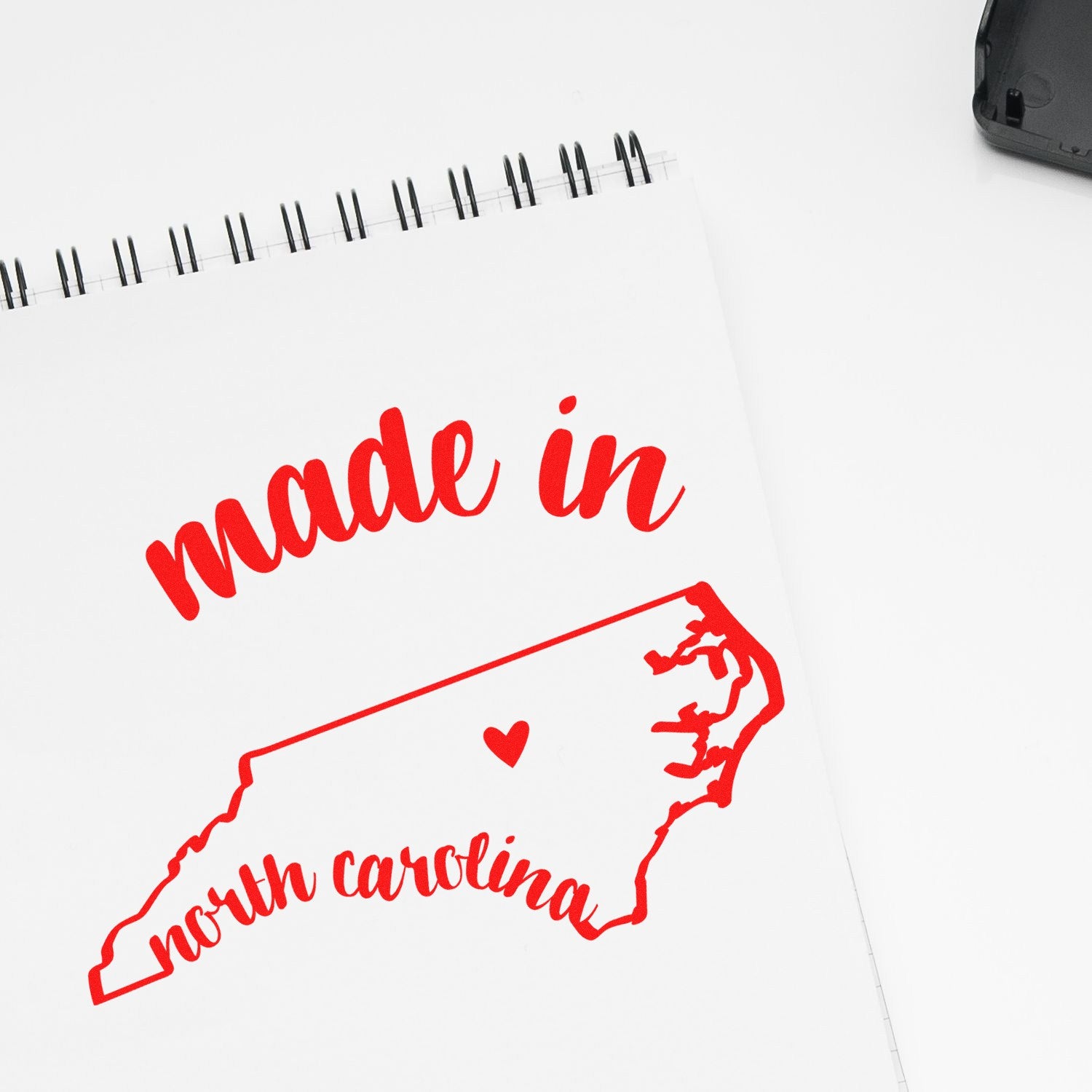 Made with Love in North Carolina Rubber Stamp featuring red text and a heart on a map outline of North Carolina, displayed on a white notepad.