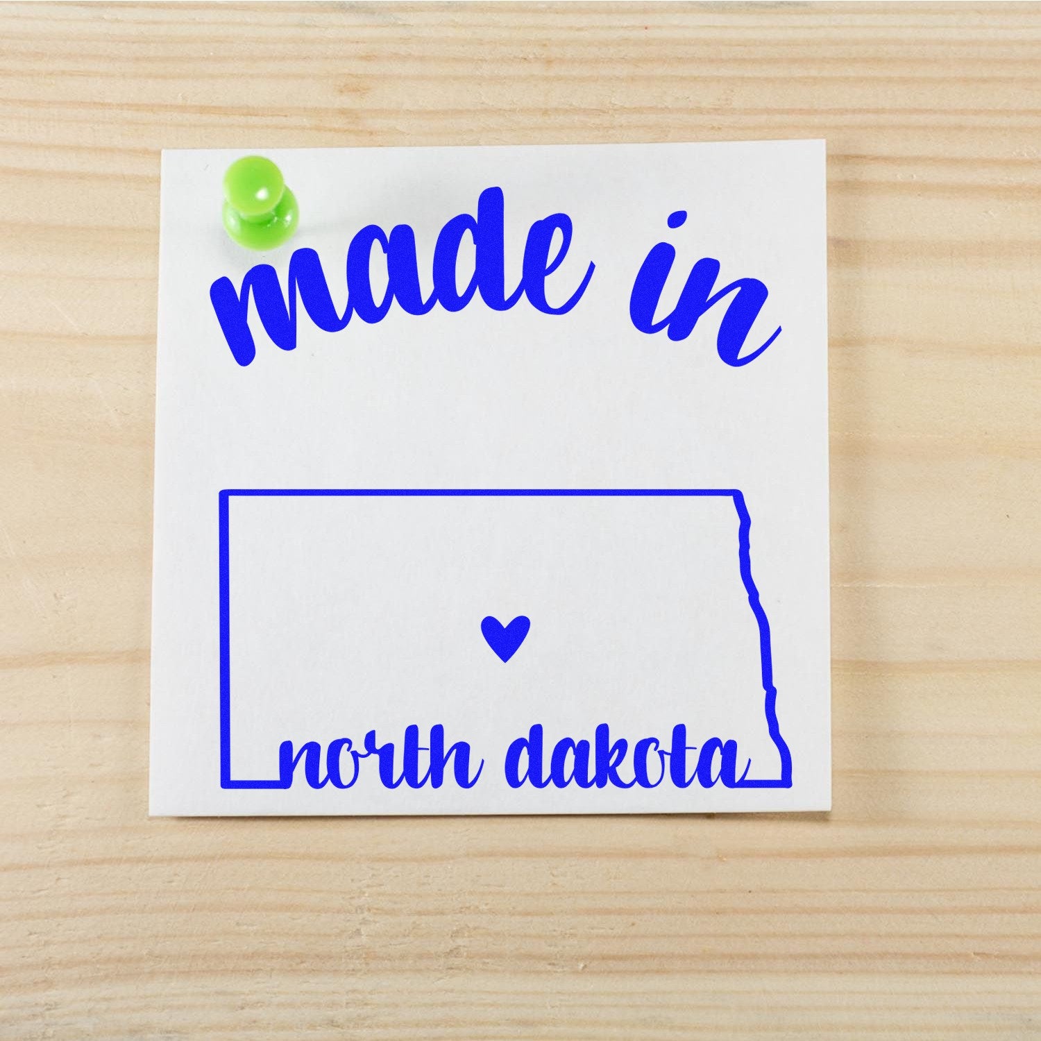 Made with Love in North Dakota Rubber Stamp featuring blue text and a heart inside the state outline on a wooden background.