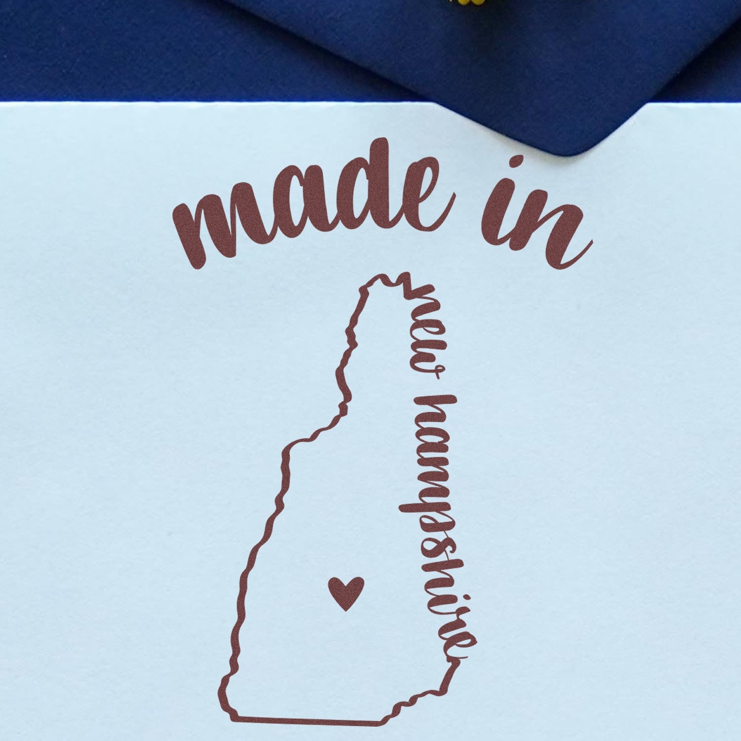 Made in New Hampshire Stamp Pre-Inked featuring a heart within the state outline and cursive text on a blue envelope.