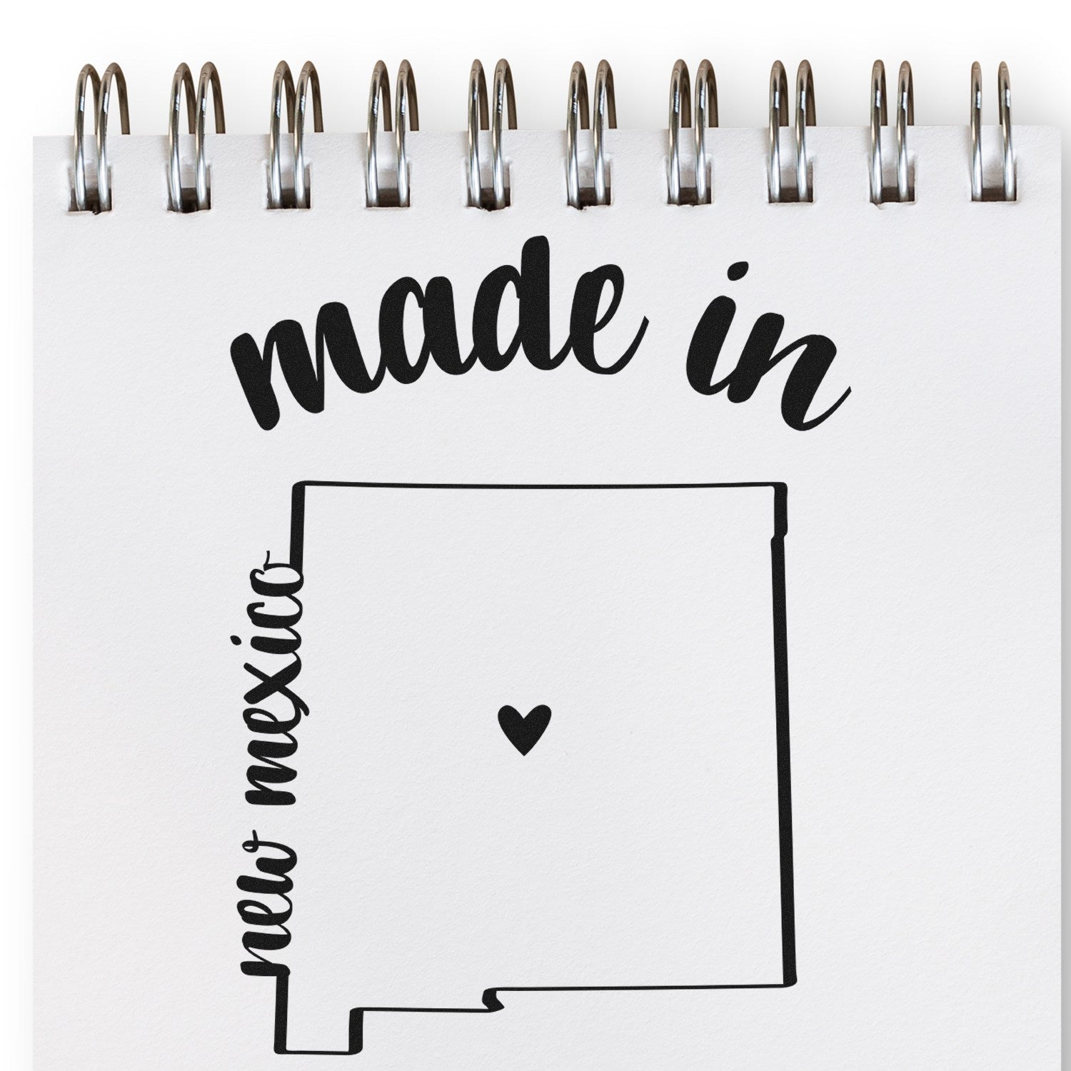 Made with Love in New Mexico Rubber Stamp featuring a heart inside the state outline, perfect for crafts and gifts. Spiral notebook background.