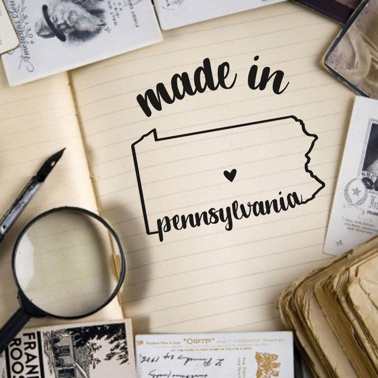 Made in Pennsylvania Stamp Pre-Inked on vintage paper background with magnifying glass and postcards, showcasing a heart within the state outline. Perfect for crafts and branding.