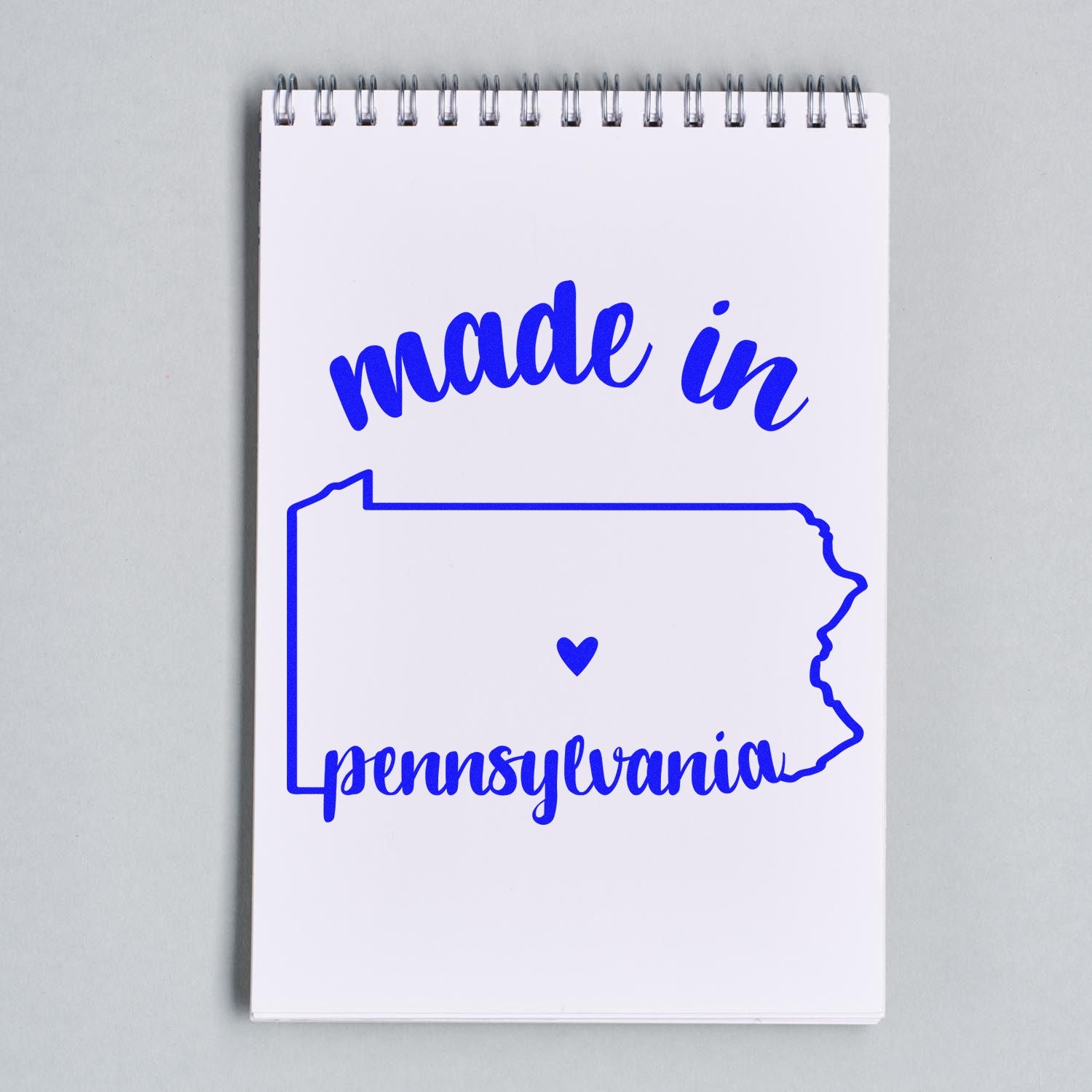 Self-Inking Handmade with Love in Pennsylvania Stamp on a notebook, featuring blue text and a heart within the state outline. Perfect for crafts and personalized projects.