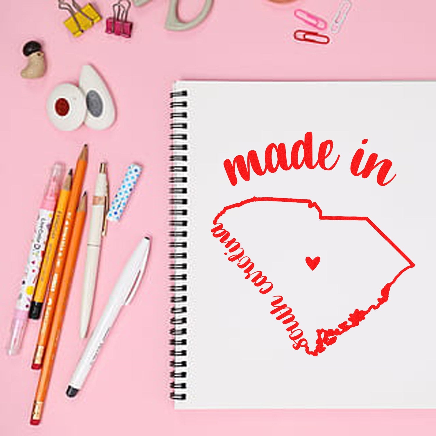 Made in South Carolina Stamp Pre-Inked, featuring a red outline of South Carolina with 'made in' text, displayed on a pink background with stationery items.