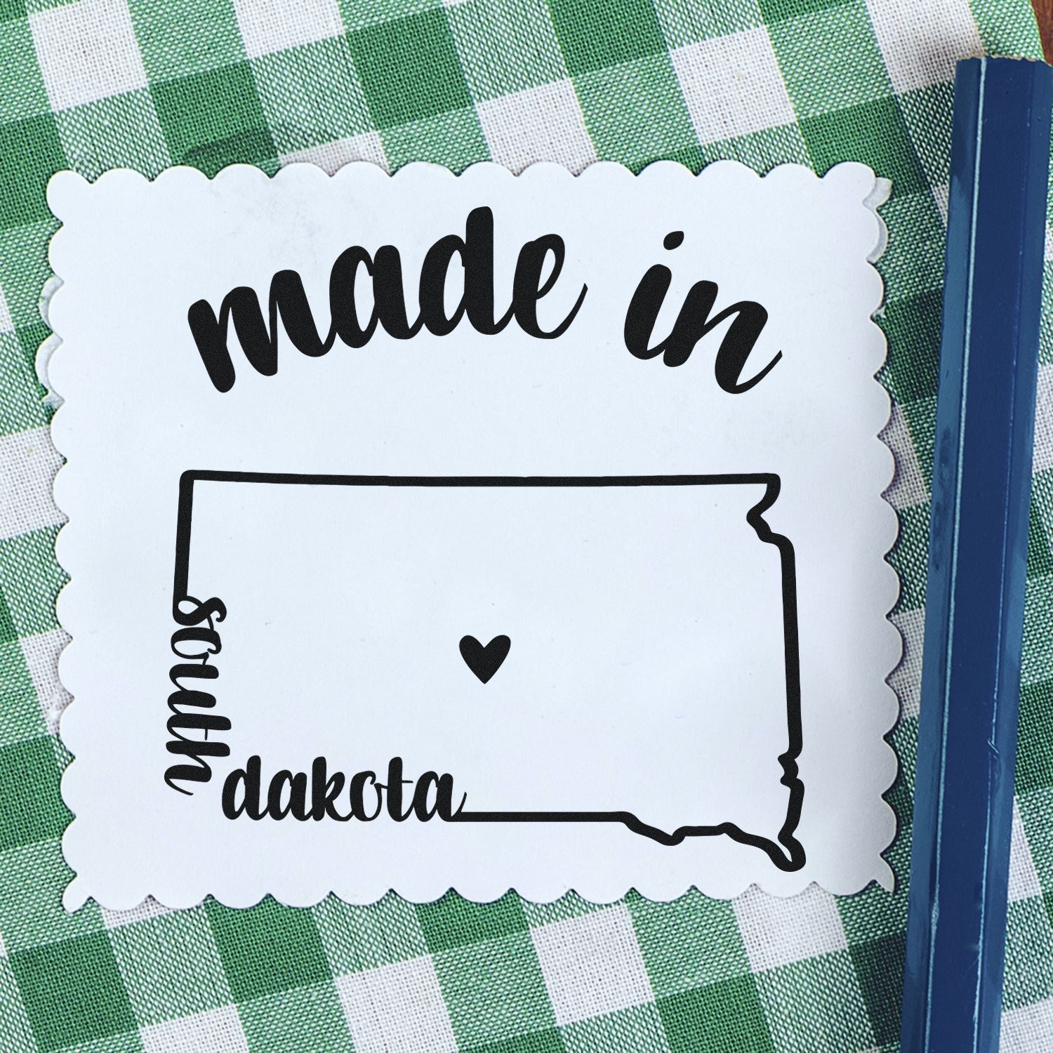 Self-Inking Handmade with Love in South Dakota Stamp on a green checkered cloth, featuring a heart within the state outline. Perfect for crafts and gifts.