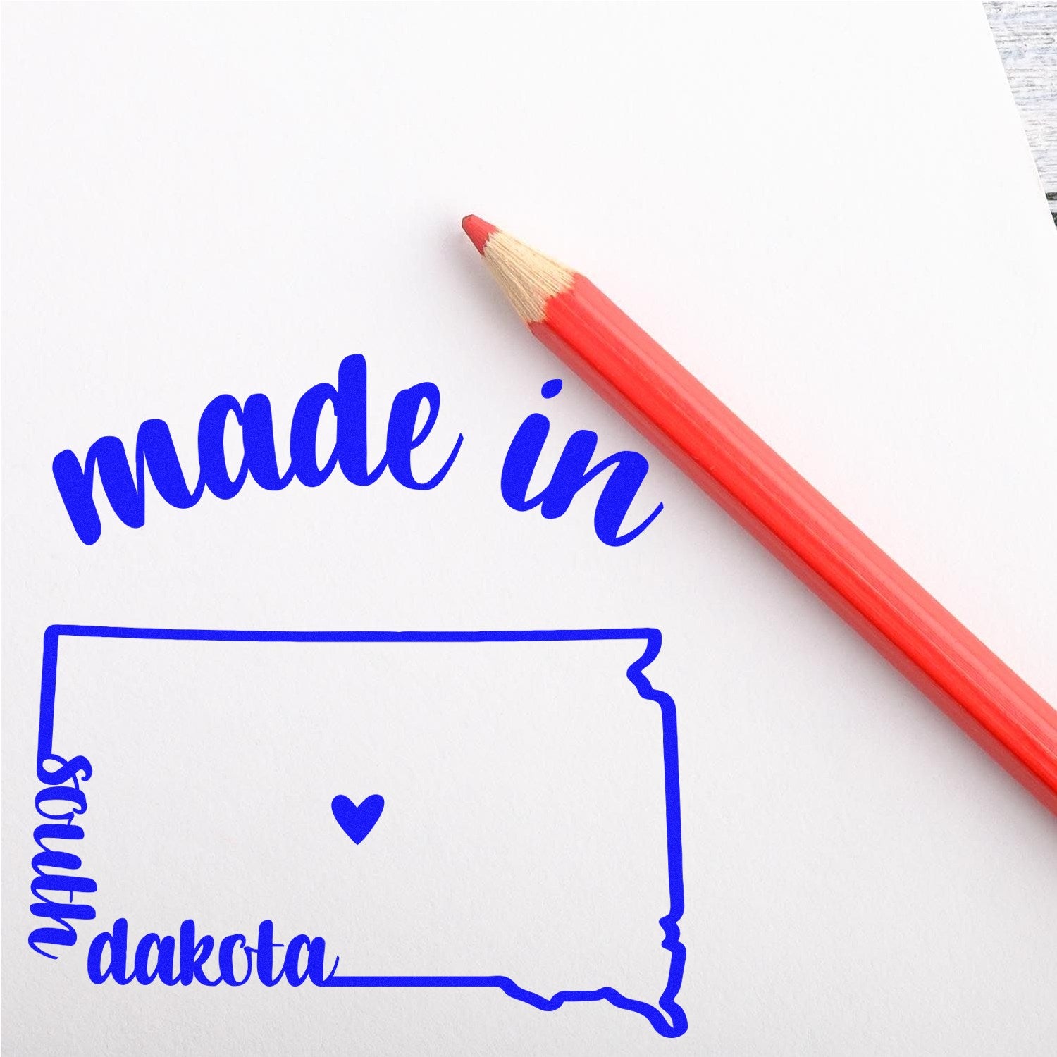 Self-Inking Handmade with Love in South Dakota Stamp featuring a blue outline of South Dakota with a heart, next to a red pencil on white paper.