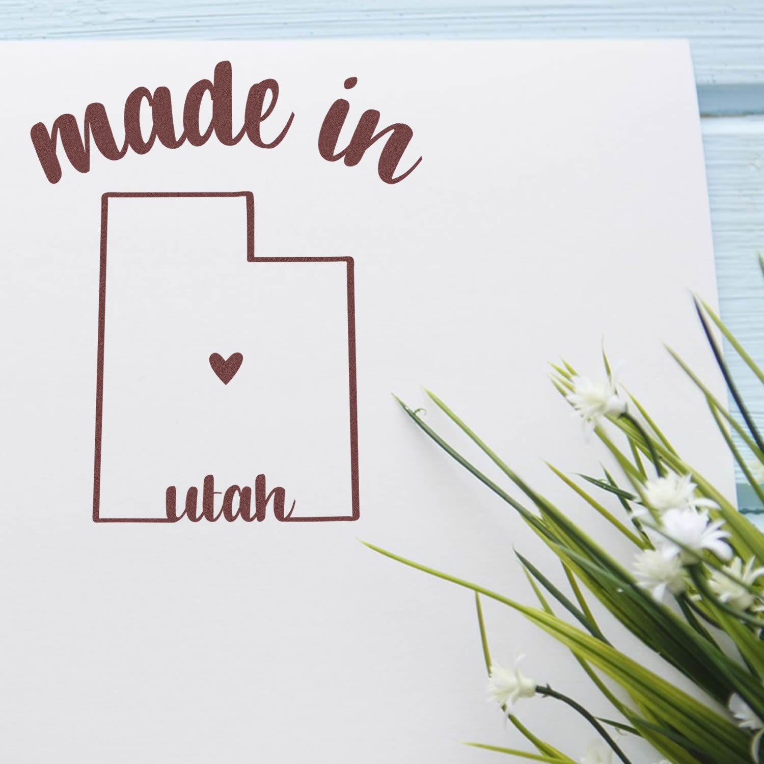 Self-Inking Handmade with Love in Utah Stamp featuring a heart inside the Utah state outline, perfect for crafts and gifts. Includes a decorative plant on a light blue background.