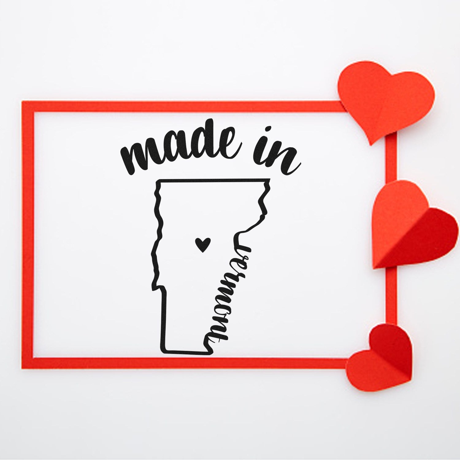 Image of the Made with Love in Vermont Rubber Stamp featuring a black outline of Vermont with a heart, surrounded by red hearts and a red frame. Perfect for crafts and personalized gifts.