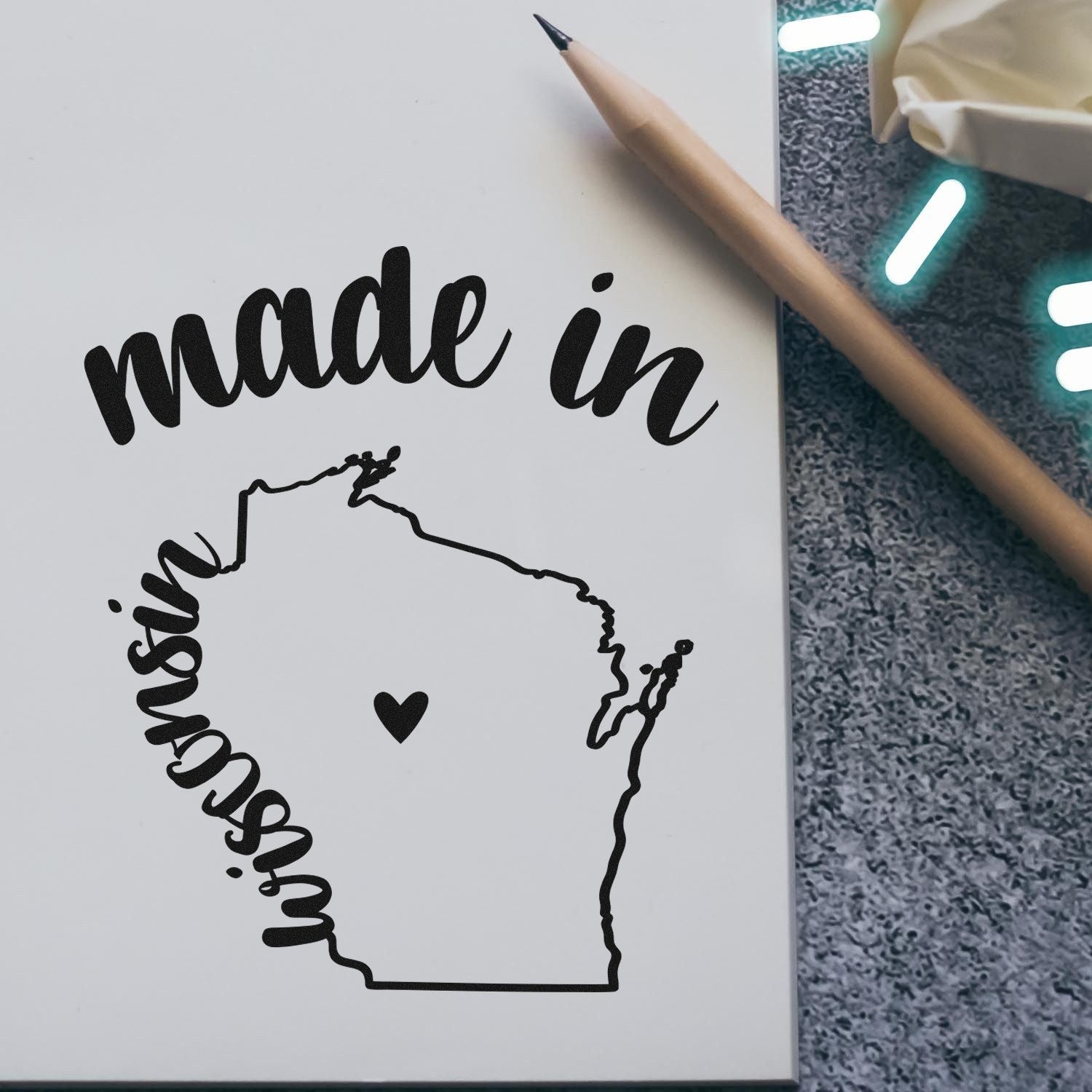 Made in Wisconsin Stamp Pre-Inked featuring a heart within the state outline and 'made in' text, displayed on paper with a pencil nearby.