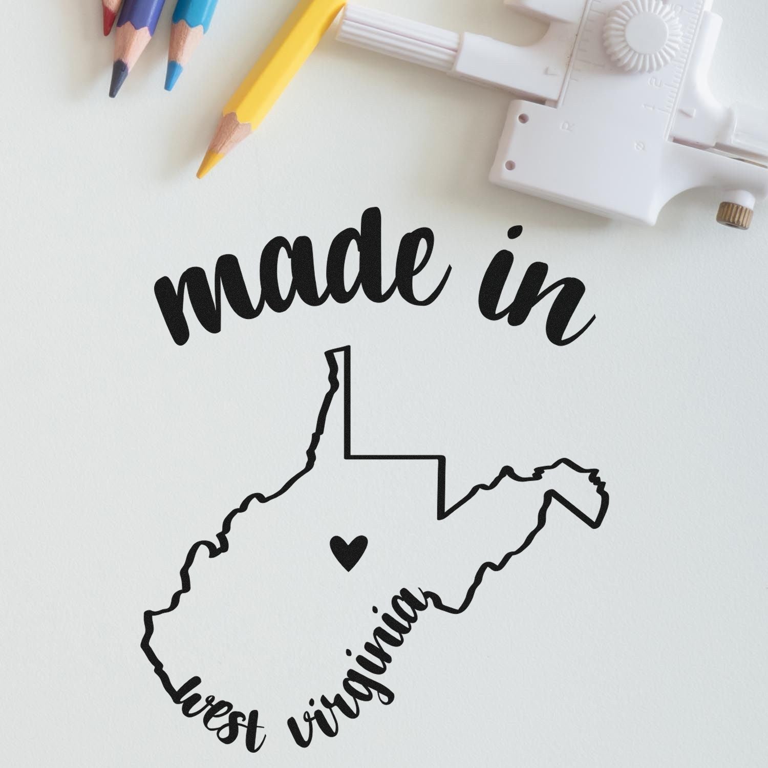 Made with Love in West Virginia Rubber Stamp featuring a heart inside the state outline, surrounded by colored pencils and a crafting tool on a light background.