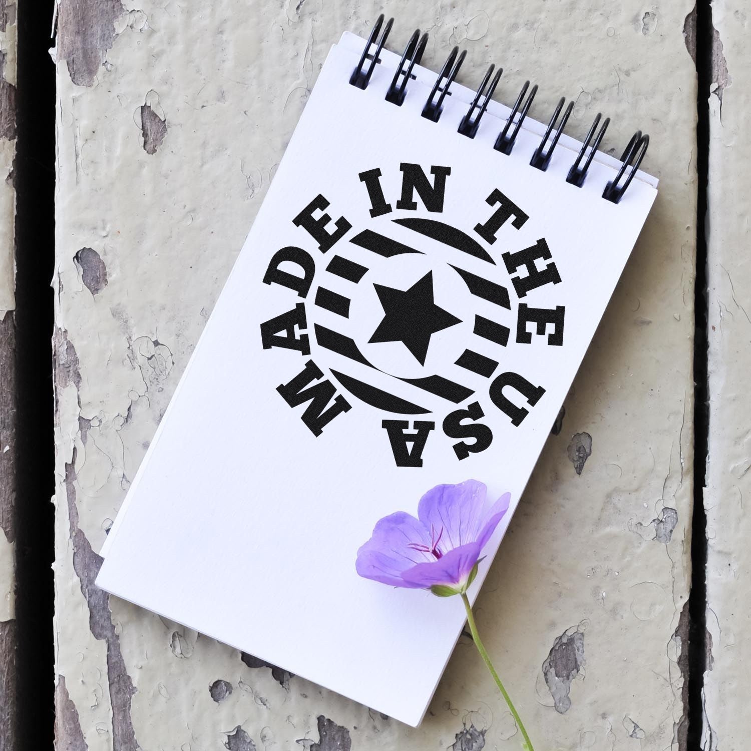 Slim Pre-Inked Made In The USA Star Emblem Stamp on a notepad with a purple flower, showcasing its crisp, bold design. Perfect for adding a patriotic touch to crafts and documents.