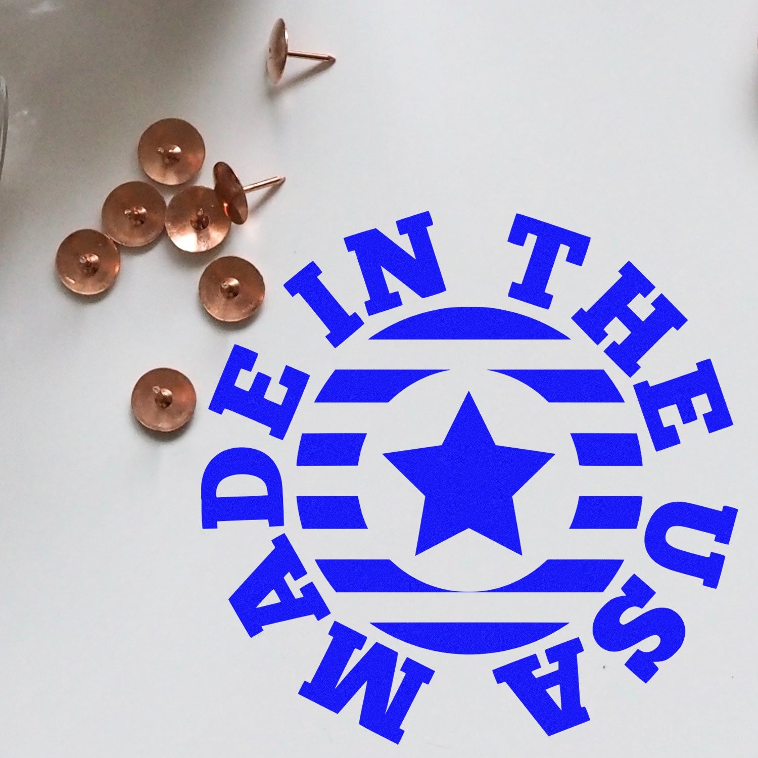 PSI Pre-Inked Made In The USA Star Emblem Stamp with blue star design, surrounded by copper tacks on a white surface.