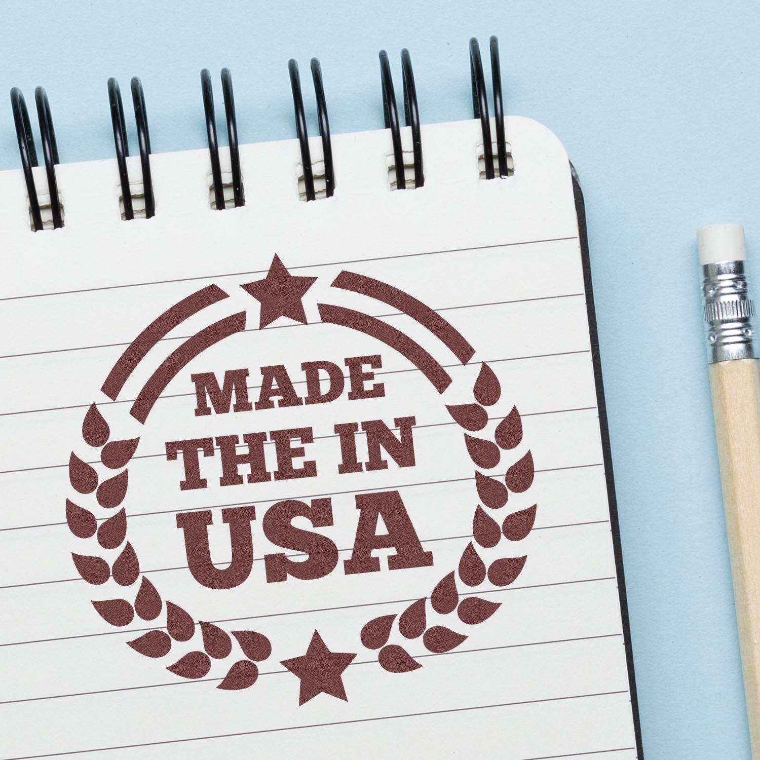 Self-Inking Made In The USA Proudly Stamp on a notebook page with a pencil, featuring a circular design with stars and laurel leaves, emphasizing American craftsmanship.