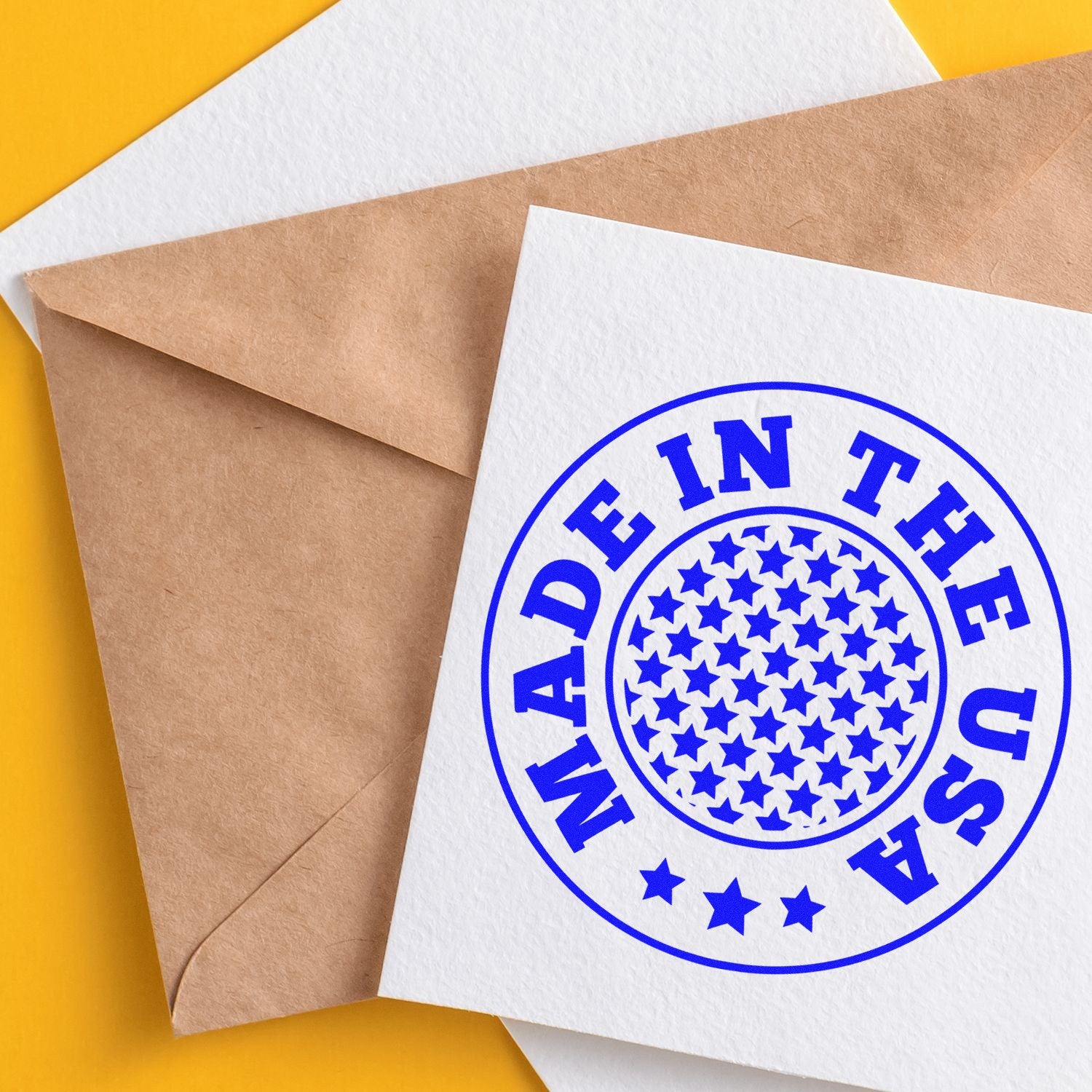 PSI Pre-Inked Stars Of America Stamp on white card with blue 'Made in the USA' design, featuring a circle of stars, placed on a brown envelope against a yellow background.