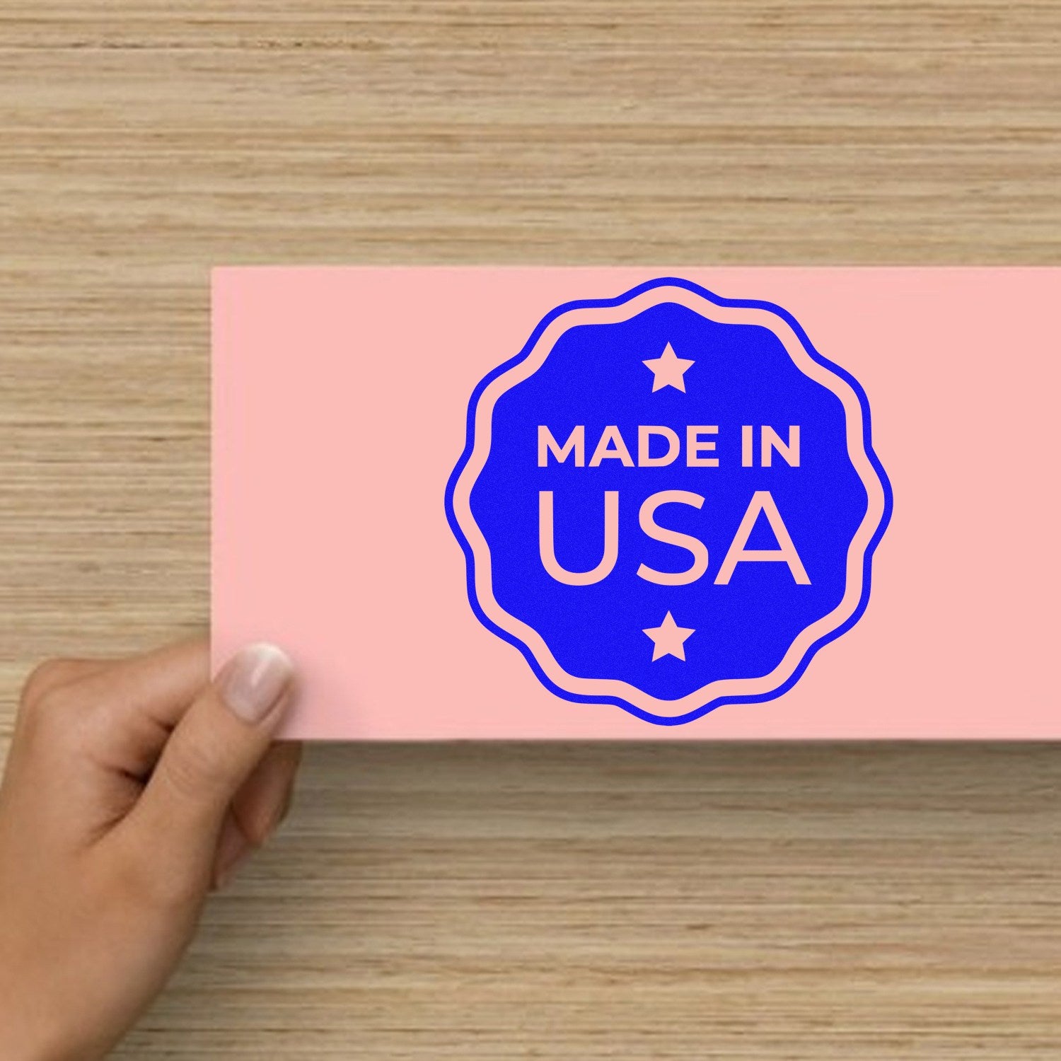 Wood Handle USA Craftsmanship Seal Rubber Stamp imprint on pink paper, showcasing 'Made in USA' design with stars, held by a hand on a wooden surface.