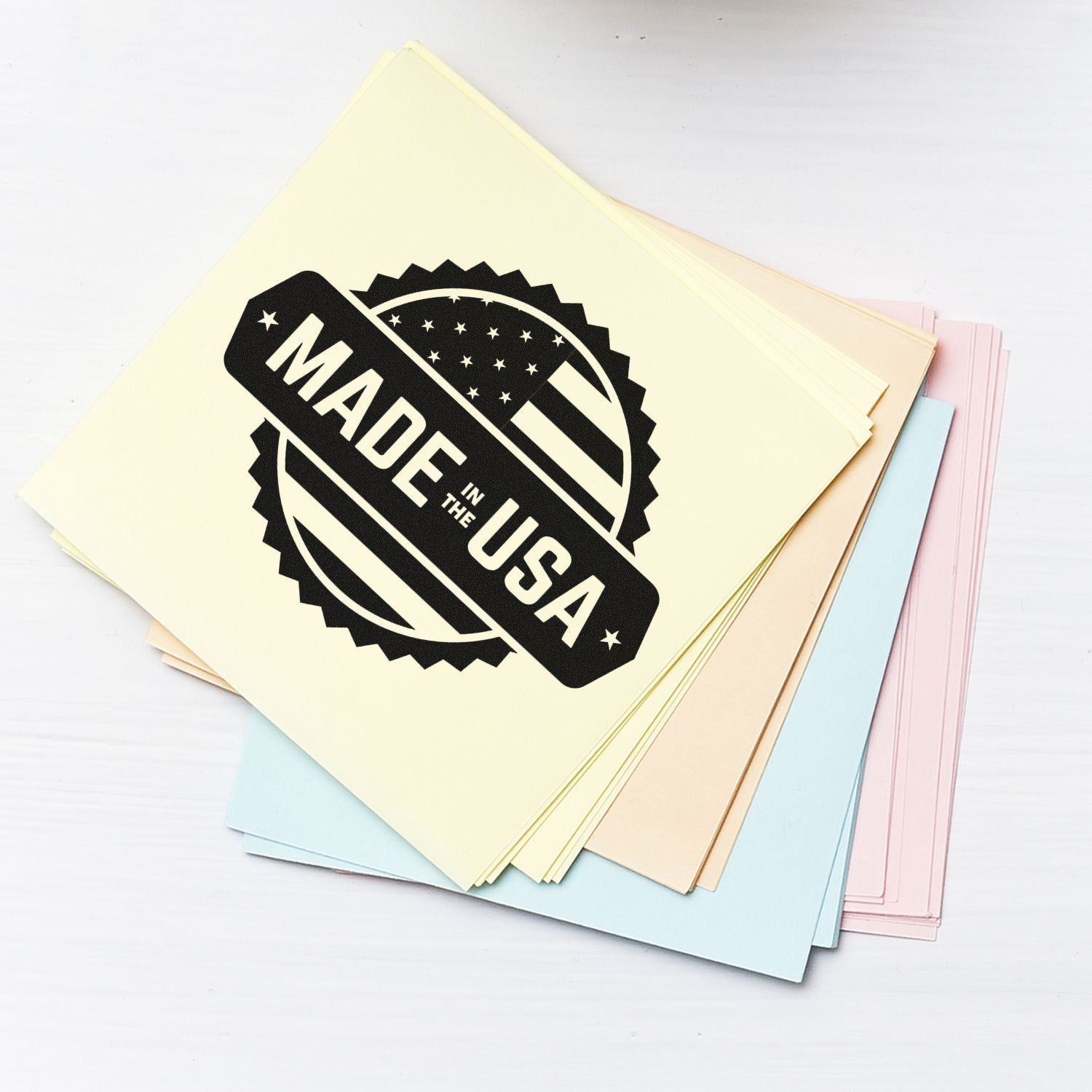 Wood Handle American Craftsmanship Seal Rubber Stamp imprint on pastel paper stack, featuring 'Made in the USA' design with stars and stripes.