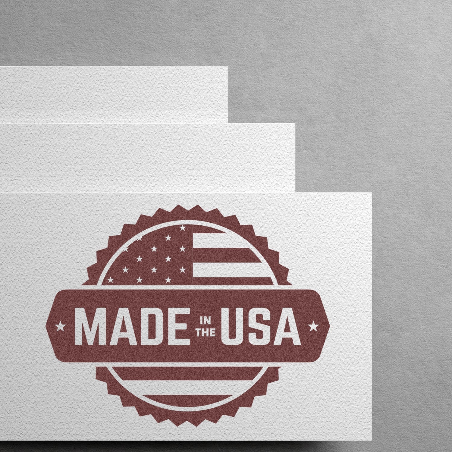 Image of the Slim Pre-Inked American Craftsmanship Seal Stamp, featuring a Made in the USA design with an American flag motif, embossed on textured white paper.