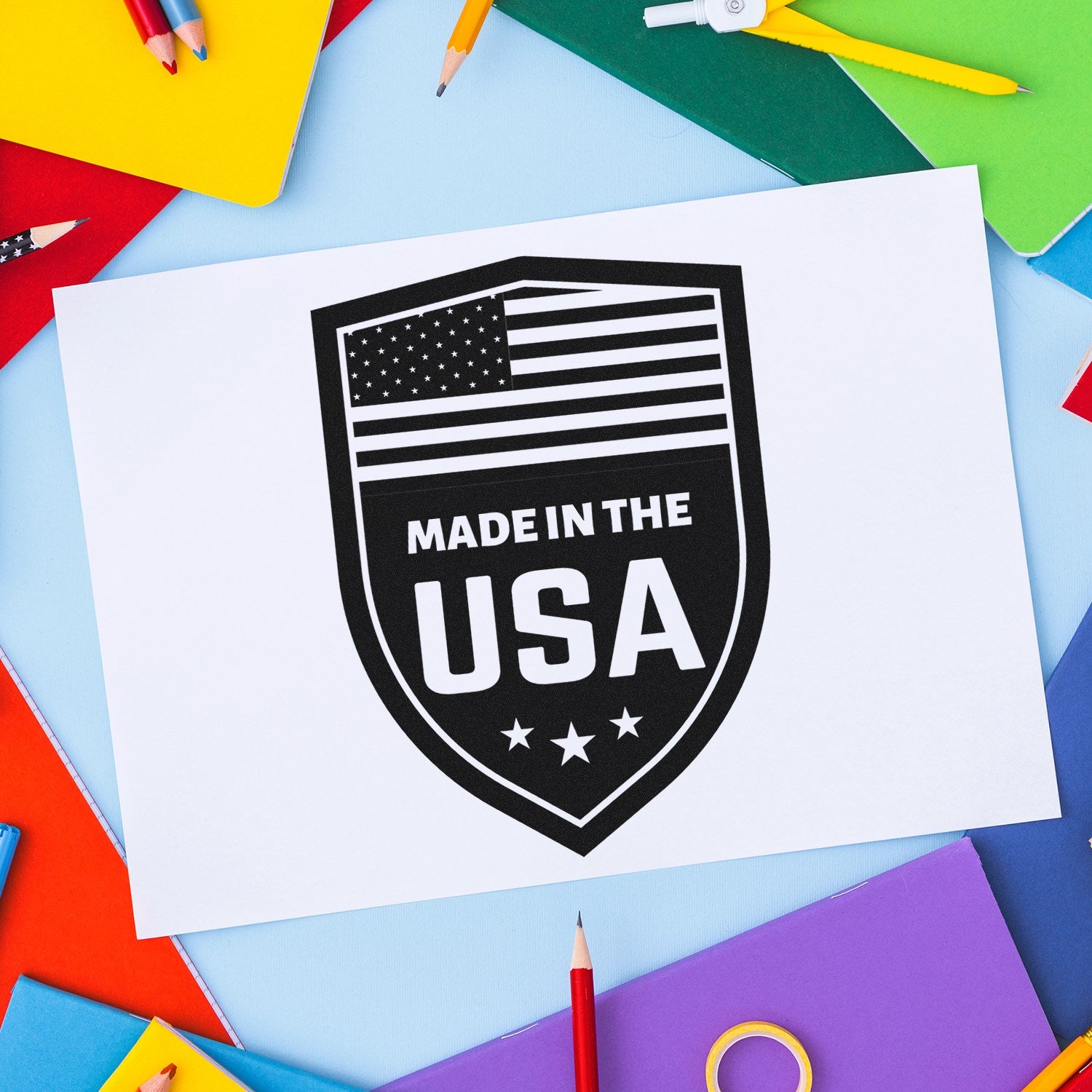 Self-Inking Proudly Made In The USA Stamp on colorful paper background, featuring a black shield design with stars and stripes, emphasizing American craftsmanship.