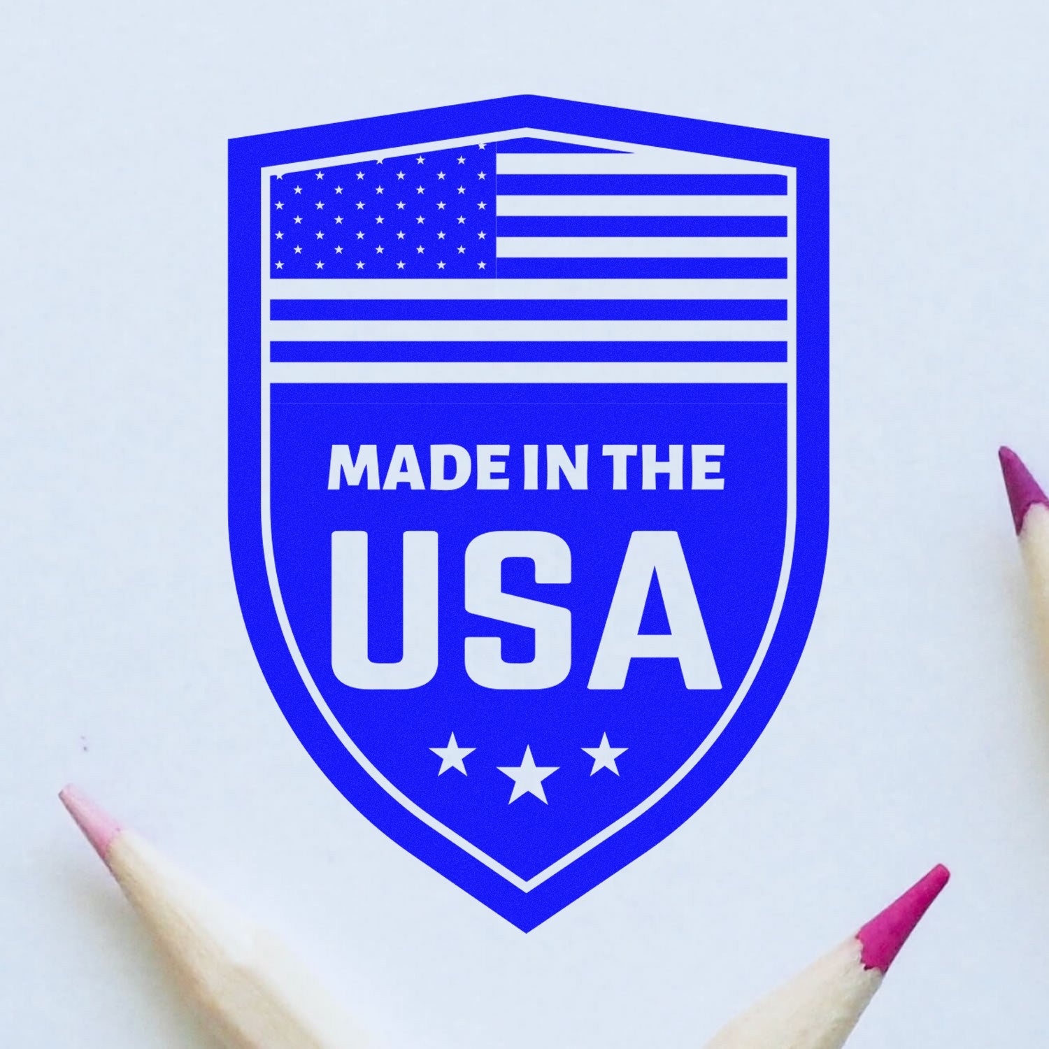 PSI Pre-Inked Proudly Made In The USA Stamp featuring a blue shield design with an American flag and Made in the USA text, surrounded by pencils on a white background.