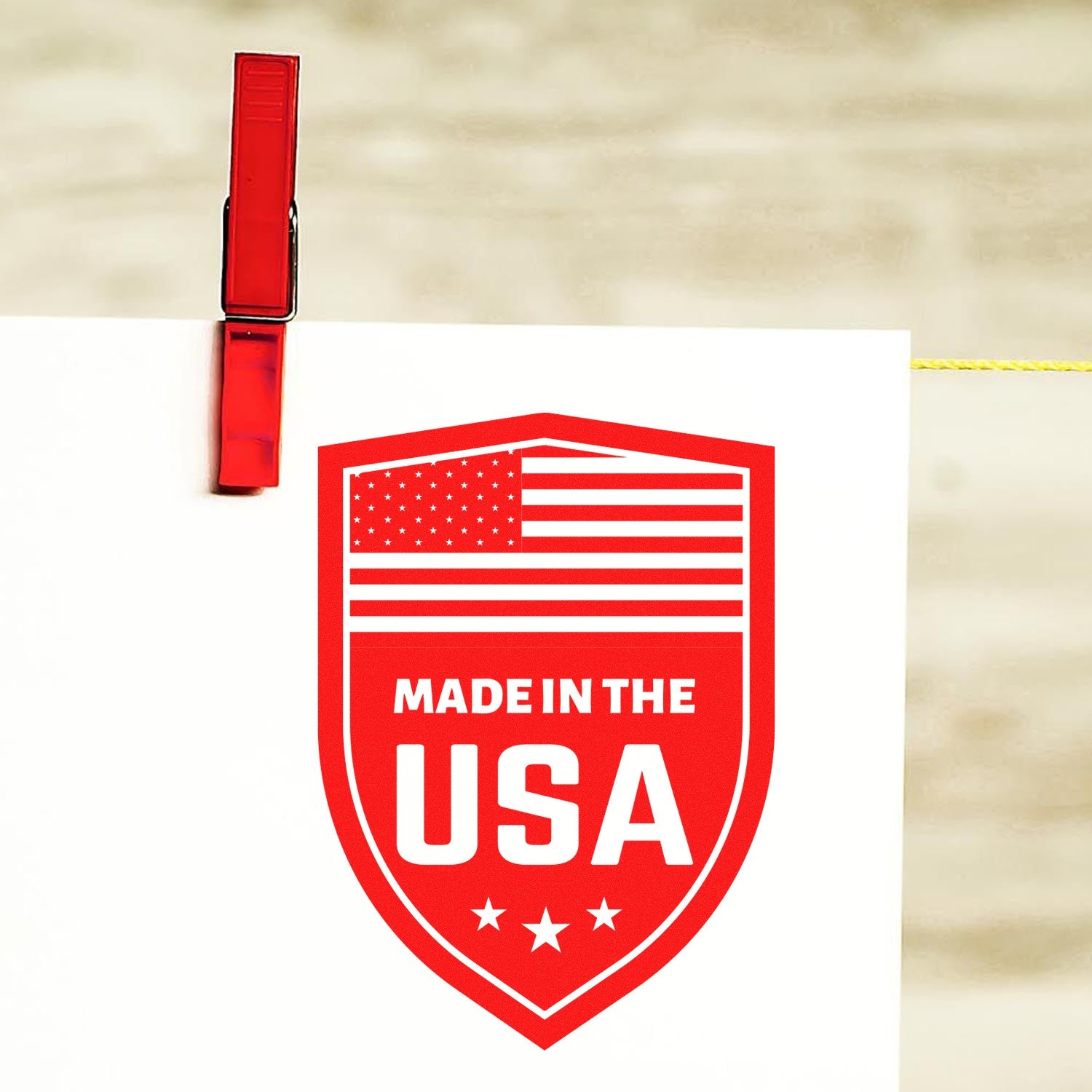 Wood Handle Proudly Made In The USA Rubber Stamp with red and white design, featuring an American flag and stars, clipped to a line with a red clothespin.