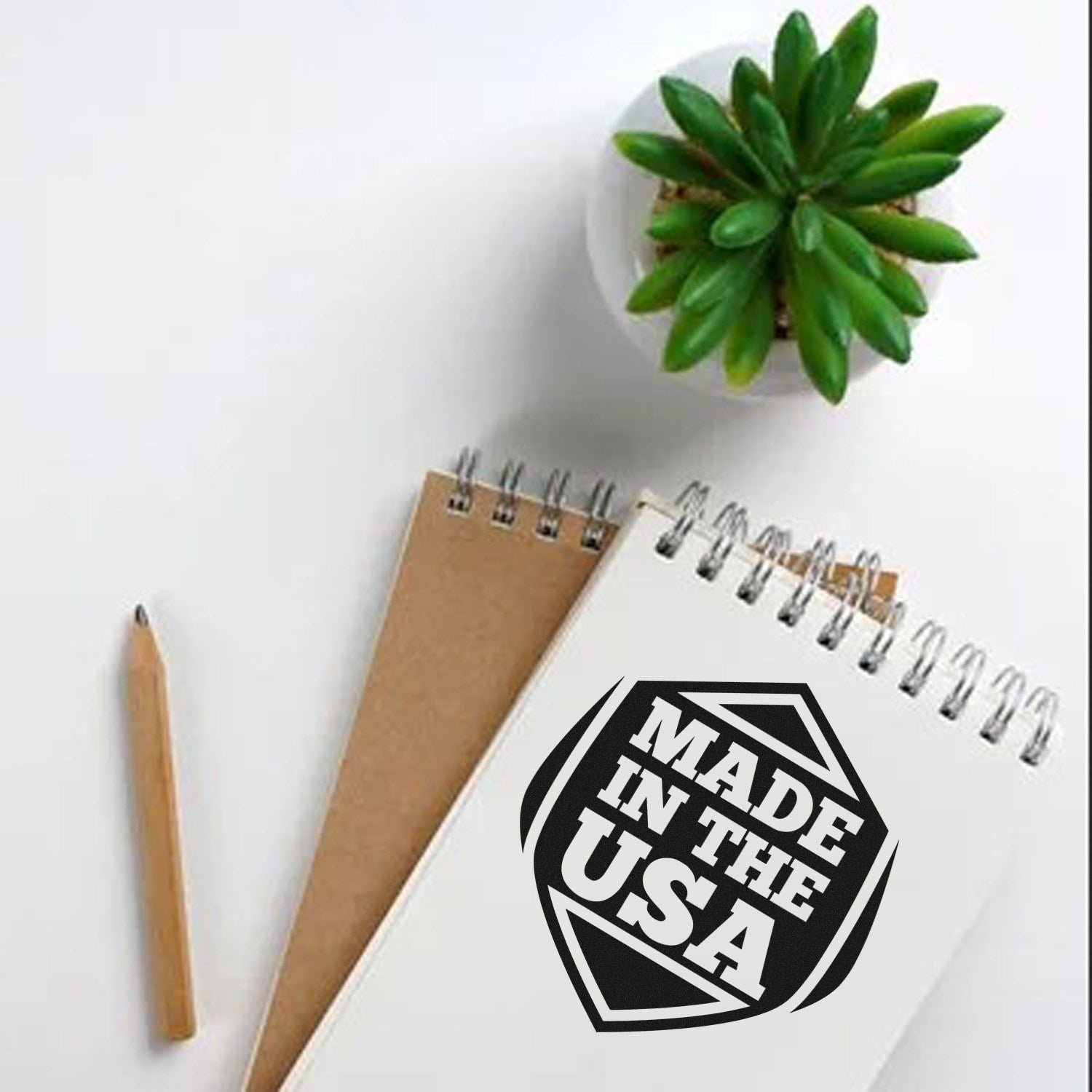 Image of the Slim Pre-Inked American Pride Seal Stamp imprint on a notepad, featuring a bold Made in the USA design, next to a pencil and a small potted plant on a white surface.