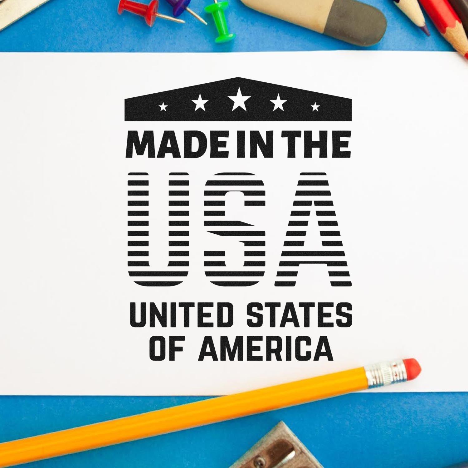 Wood Handle Patriotic Pride Rubber Stamp imprint reading 'Made in the USA' with stars, displayed on white paper, surrounded by colorful office supplies.