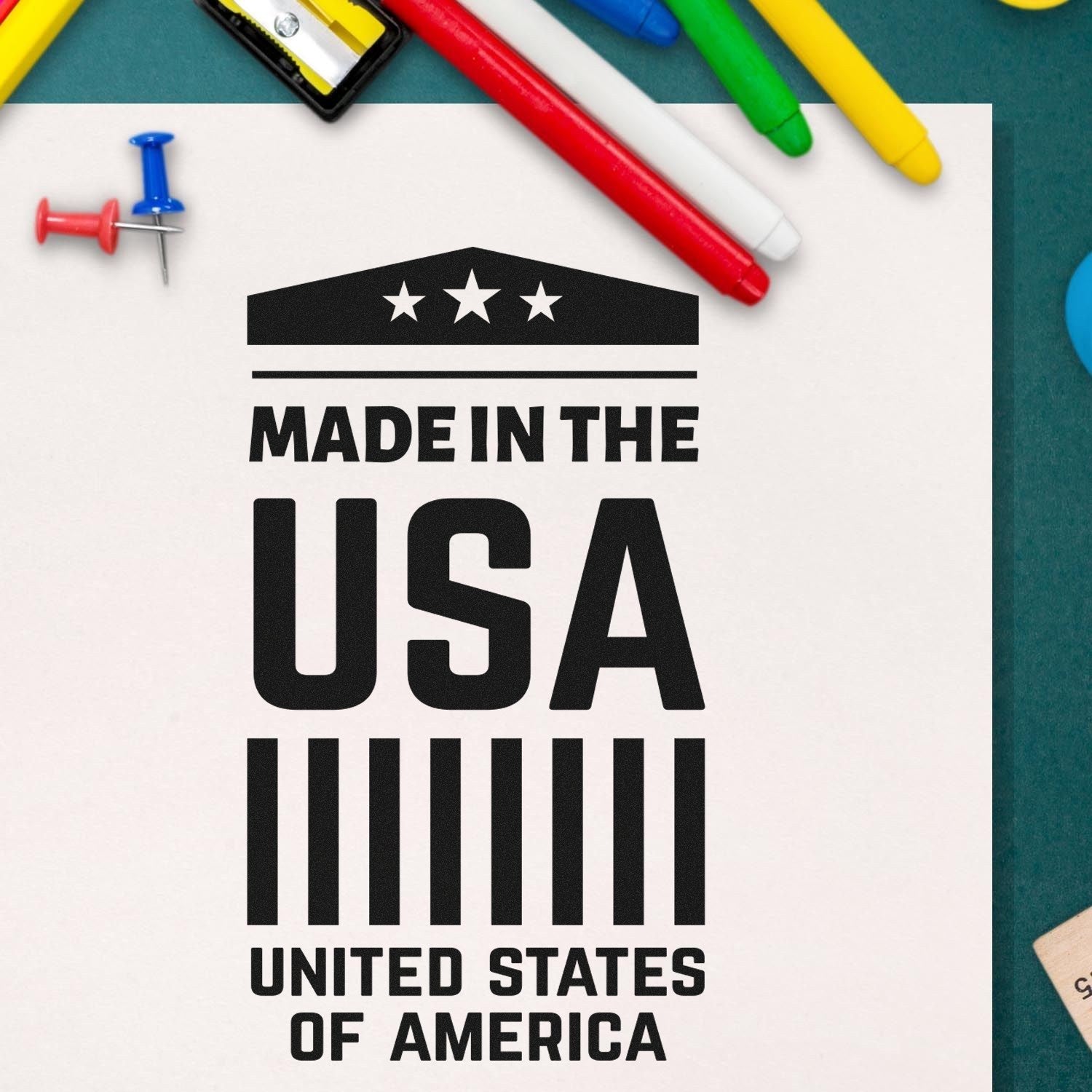 Self-Inking American Pride Emblem Stamp featuring Made in the USA text with stars and stripes design, surrounded by colorful office supplies on a green background.