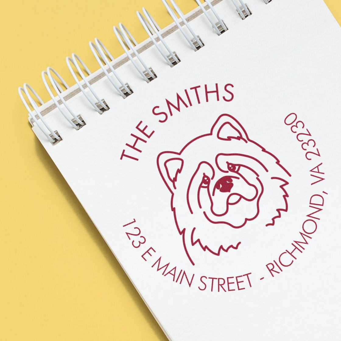 Red bear seal stamp on white spiral notebook reading The Smiths, with address details on a yellow background.