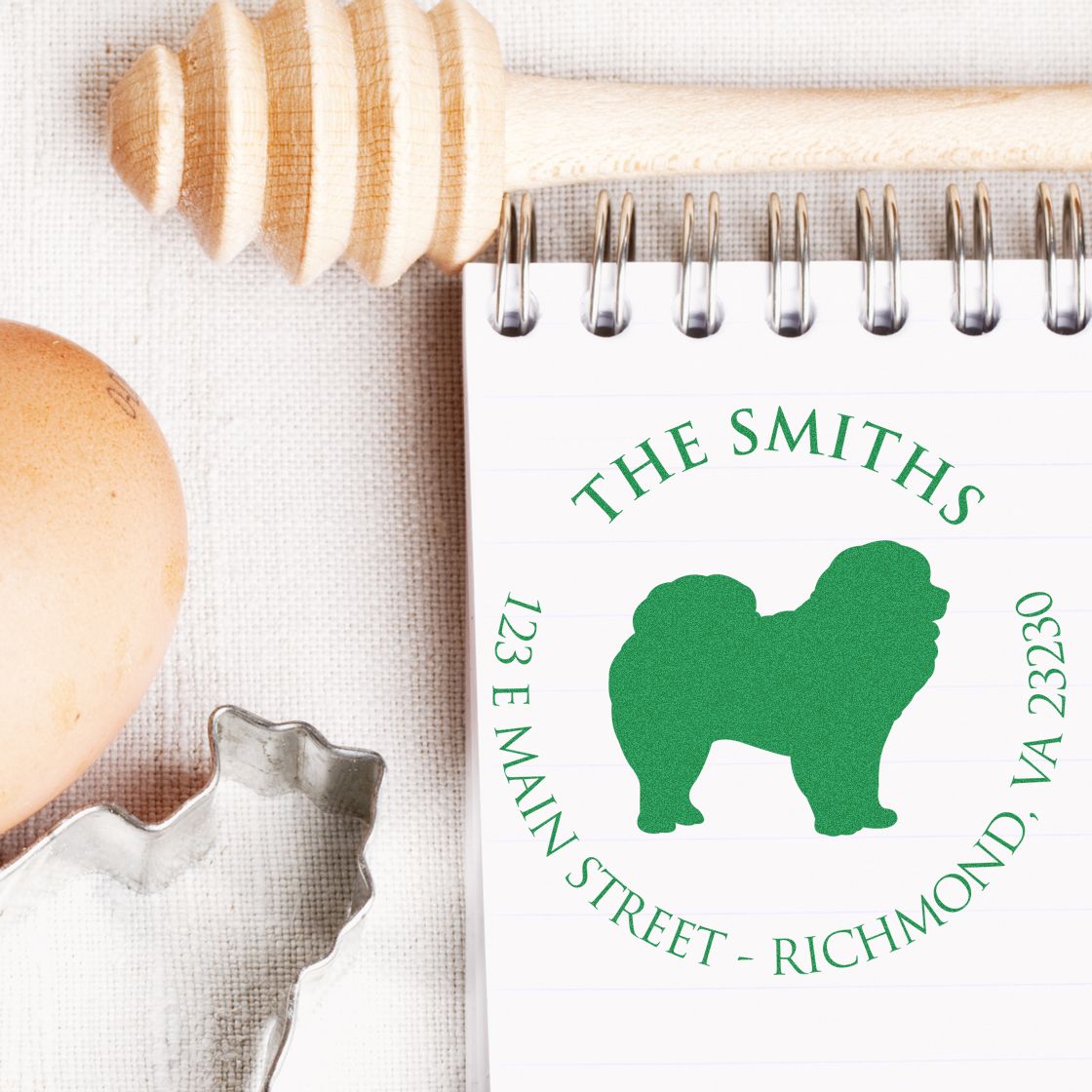 Green custom stamp seal for The Smiths with dog silhouette on notebook, beside a wooden embosser and metal cutter.