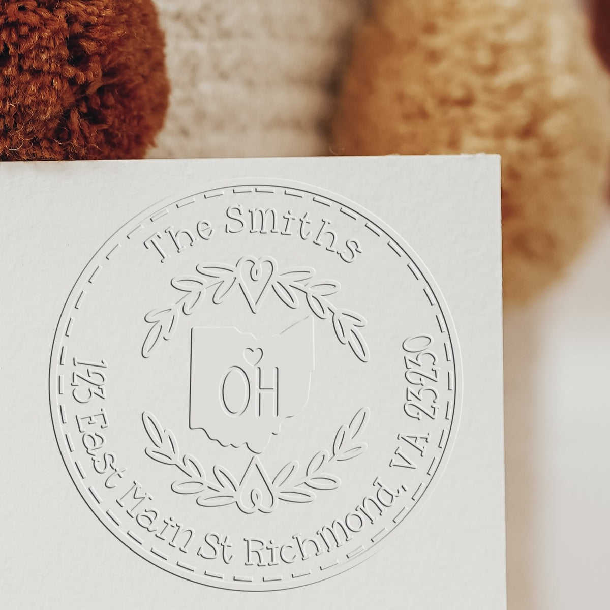 White embossed custom stamp seal with circular wreath, Ohio outline, and The Smiths text on paper against warm brown background
