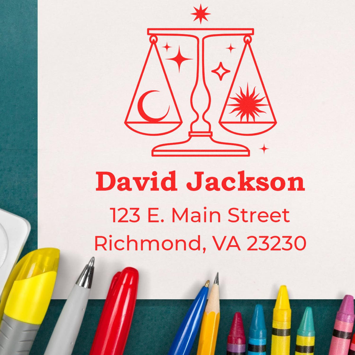 Red custom seal stamp with balance scale, crescent moon and sun logo, David Jackson address on white paper, colorful pens.