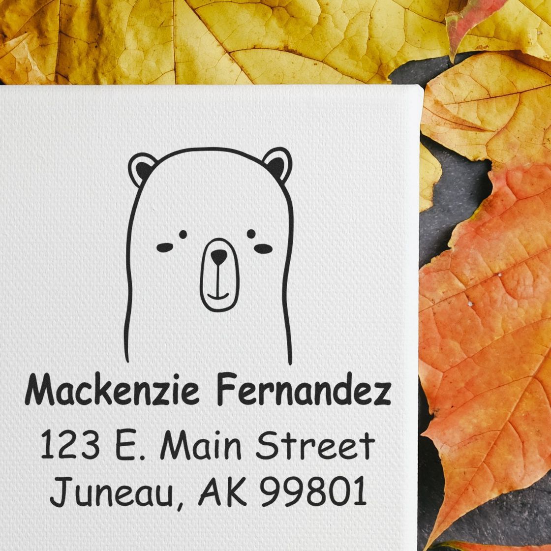 Wood handle adorable bear cartoon animal made to order mail stamp on a canvas with personalized new address stamp reading "Mackenzie Fernandez, 123 E. Main Street, Juneau, AK 99801" against a background of autumn leaves.
