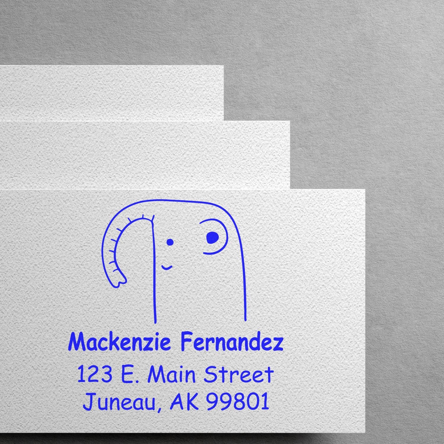 Endearing elephant cartoon animal design on a custom-made return mail stamp with a wood handle. The address stamper features "Mackenzie Fernandez, 123 E. Main Street, Juneau, AK 99801" in blue ink, showcasing a made-to-order address stamp.