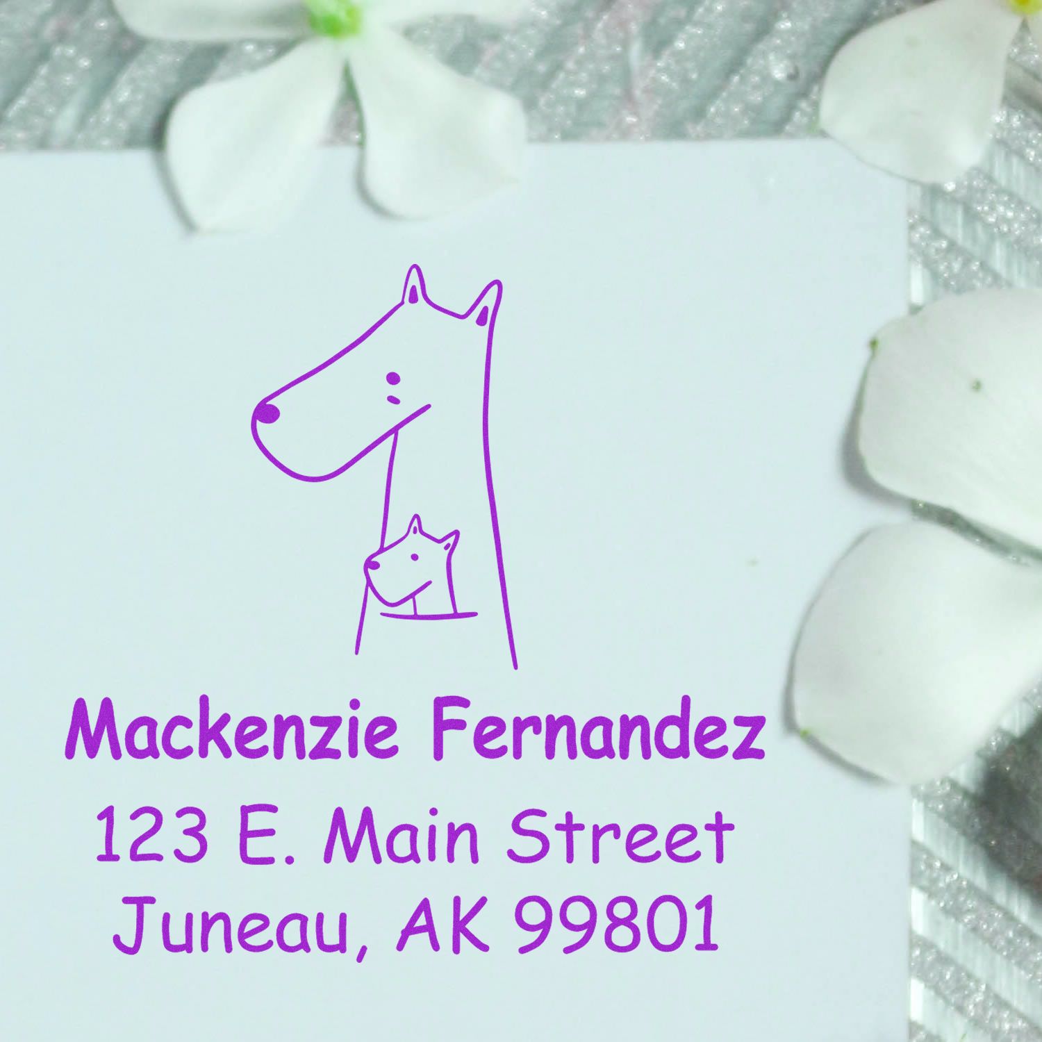 Portable Pre-Inked Snuggly Kangaroos Custom Designed Mailing Stamper in use, featuring a Custom Address Stamp with a kangaroo illustration. The stamp displays the name Mackenzie Fernandez and address 123 E. Main Street, Juneau, AK 99801 on a white card with flower petals.