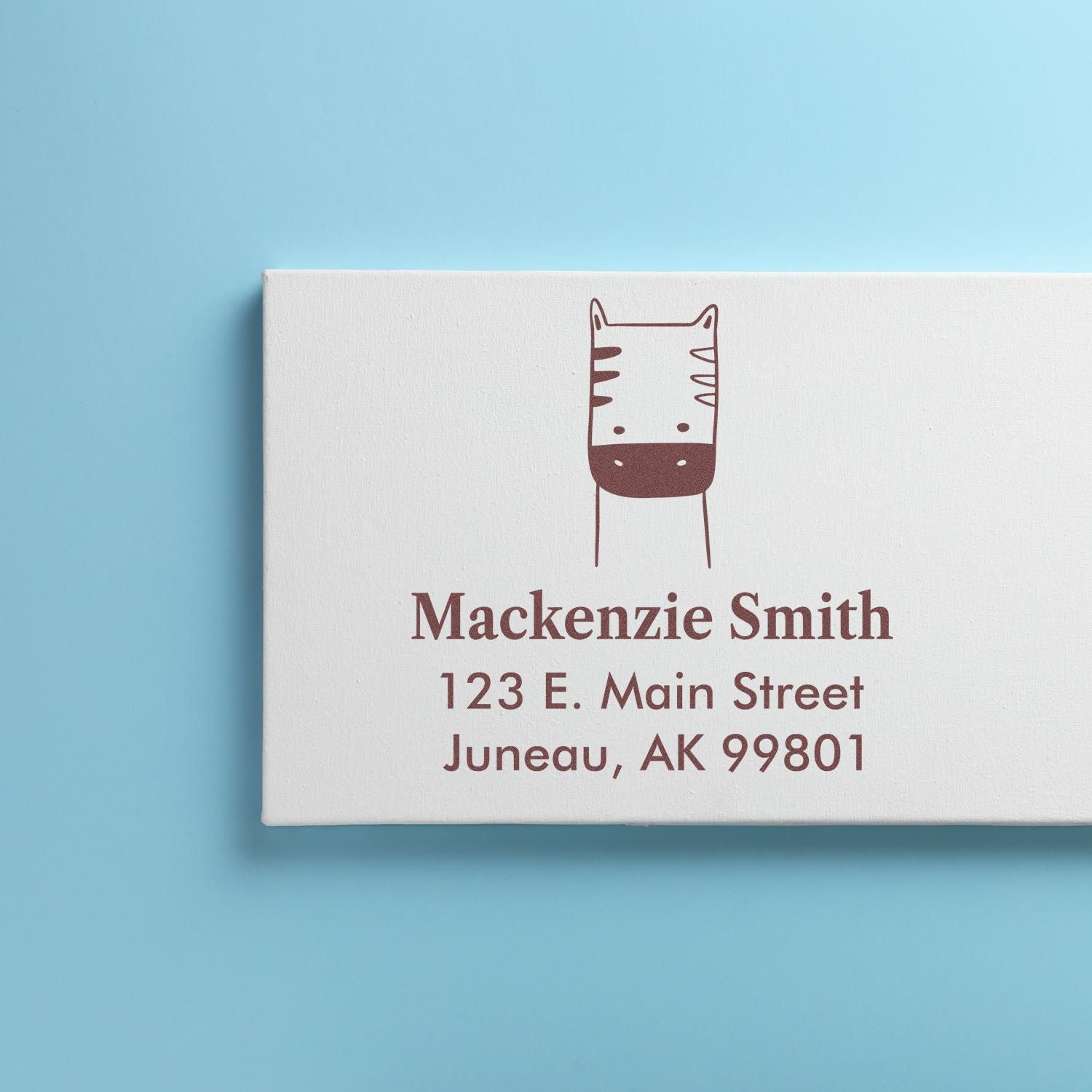 Wood handle frolicsome zebra cartoon animal made to order envelope stamp displayed on a custom home stamp. The stamp features a playful zebra design above the name and address "Mackenzie Smith, 123 E. Main Street, Juneau, AK 99801" on a light blue background.