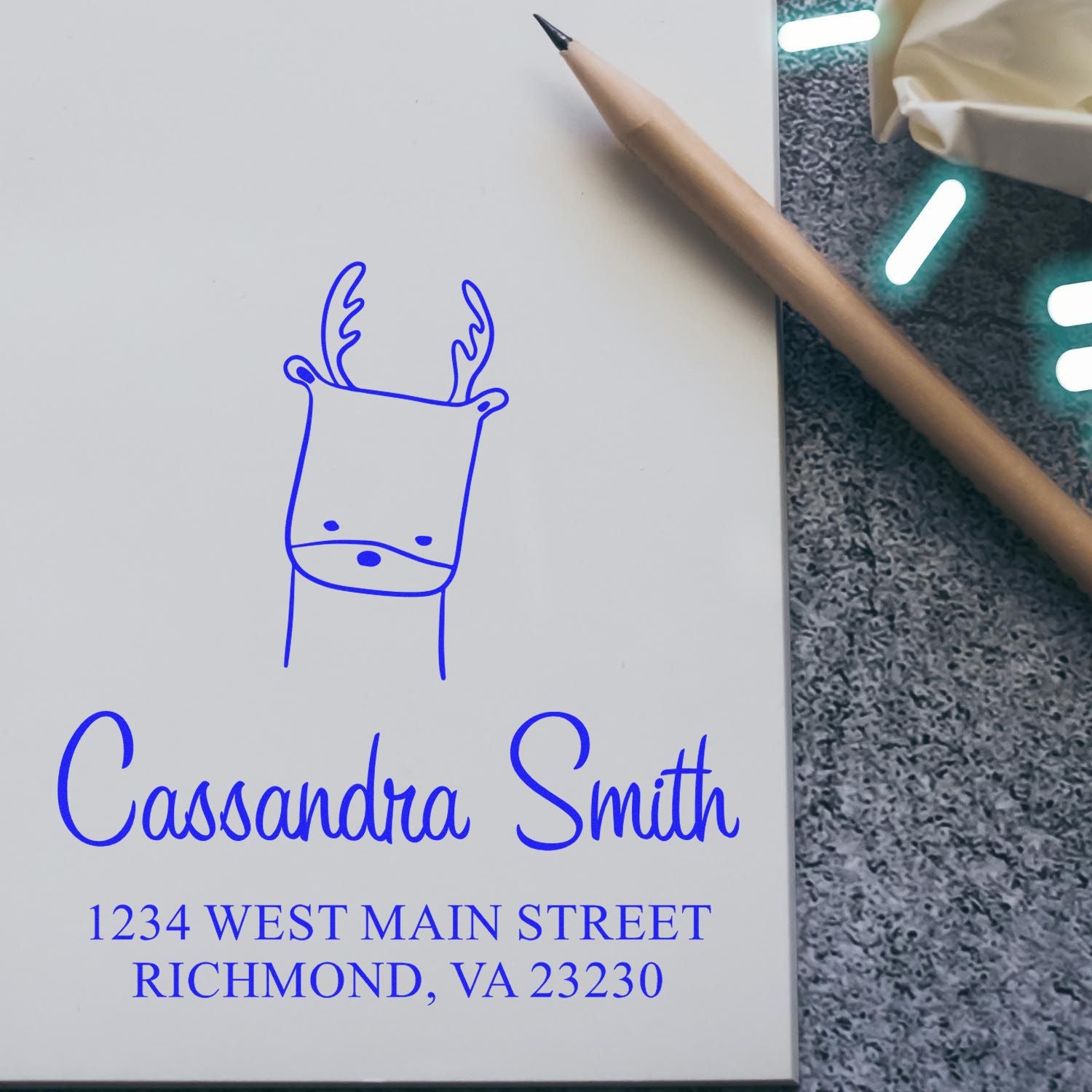 Self-inking stamp featuring a cartoon animal, a regal reindeer, on a custom-made envelope. The design includes "Cassandra Smith" and "1234 West Main Street, Richmond, VA 23230." This customized home stamp adds a personal touch to stationery.