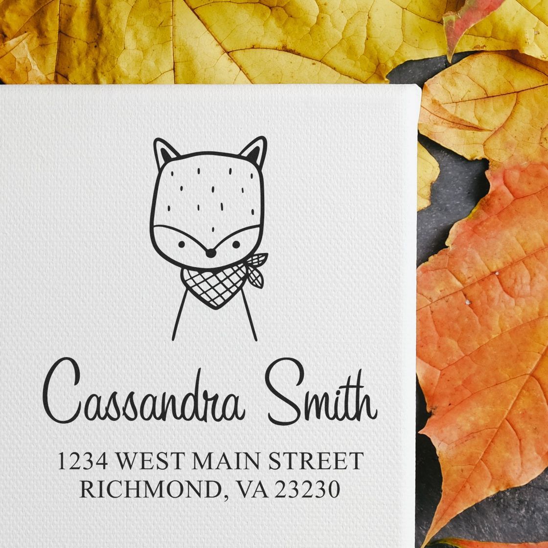 Wood handle fancy fox cartoon animal made to order return address stamp on a white card with customizable mailing stamp design. The card displays a fox illustration above the name "Cassandra Smith" and an address, set against a background of autumn leaves.
