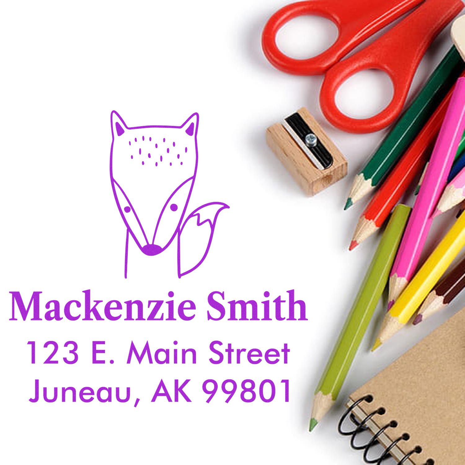 Fast Fox Pre-Inked Customized Home Address Stamp displayed with colorful pencils, scissors, and a sharpener. The Custom Home Stamper shows the name "Mackenzie Smith" and address "123 E. Main Street, Juneau, AK 99801" in purple text next to a fox illustration.