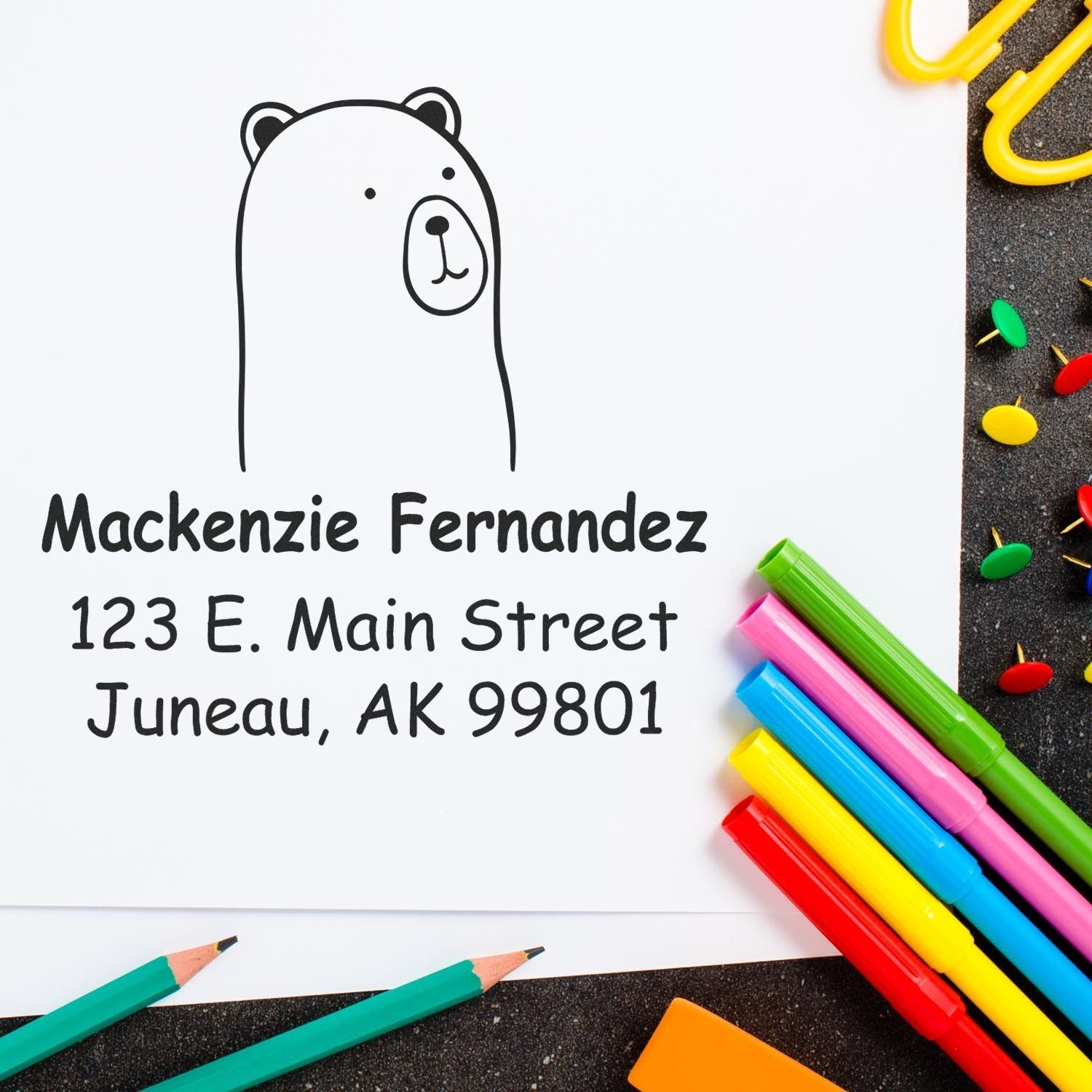 Wood handle cuddly polar bear cartoon animal made to order new home stamper on paper. Custom new address stamp with "Mackenzie Fernandez, 123 E. Main Street, Juneau, AK 99801" surrounded by colorful pens and paperclips.