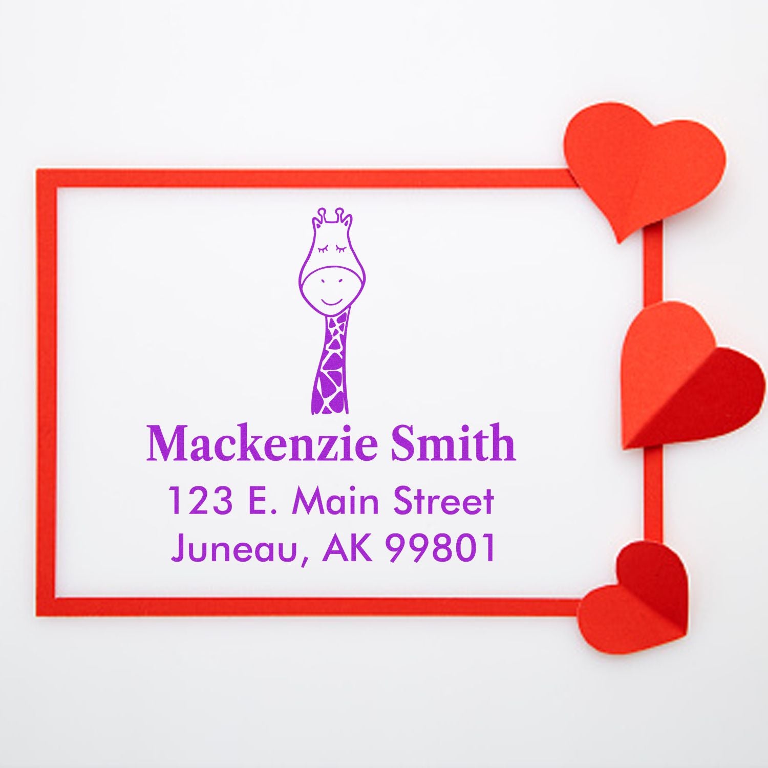 Portable Pre-Inked Jolly Giraffe Custom Designed New Home Stamp featuring a purple giraffe illustration and personalized return mail stamp with the name Mackenzie Smith and address 123 E. Main Street, Juneau, AK 99801, framed by red hearts.