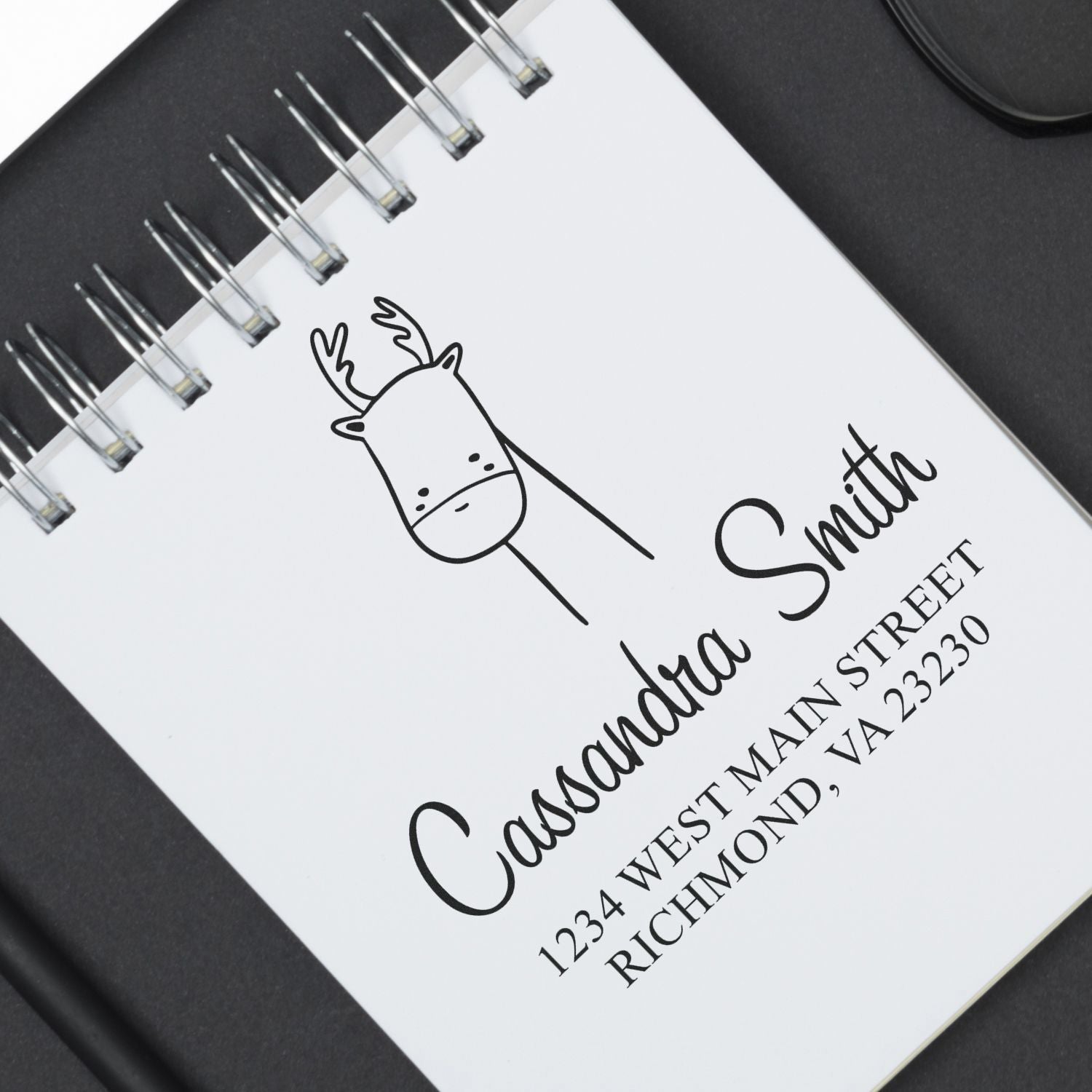 Wood Handle Darling Deer Cartoon Animal Custom Mailing Stamper used on a notebook page. The design features a cute deer illustration above the text "Cassandra Smith, 1234 West Main Street, Richmond, VA 22330." Personalizable Return Mail Stamp.
