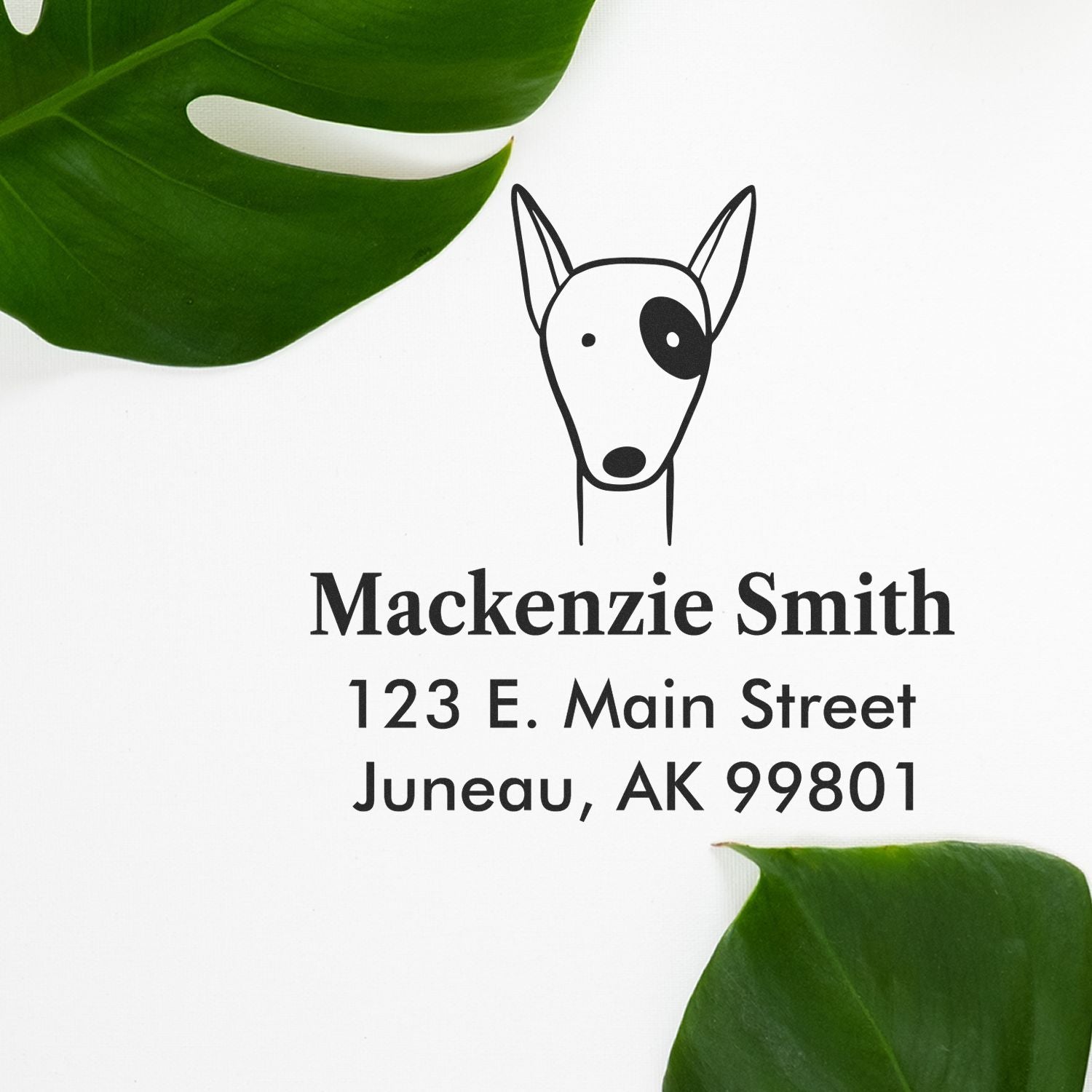 Wood Handle Delightful Dog Cartoon Animal Custom Home Stamper used on white paper with green leaves. The Personalized Home Stamp features a simple dog illustration above the name "Mackenzie Smith" and address "123 E. Main Street, Juneau, AK 99801".